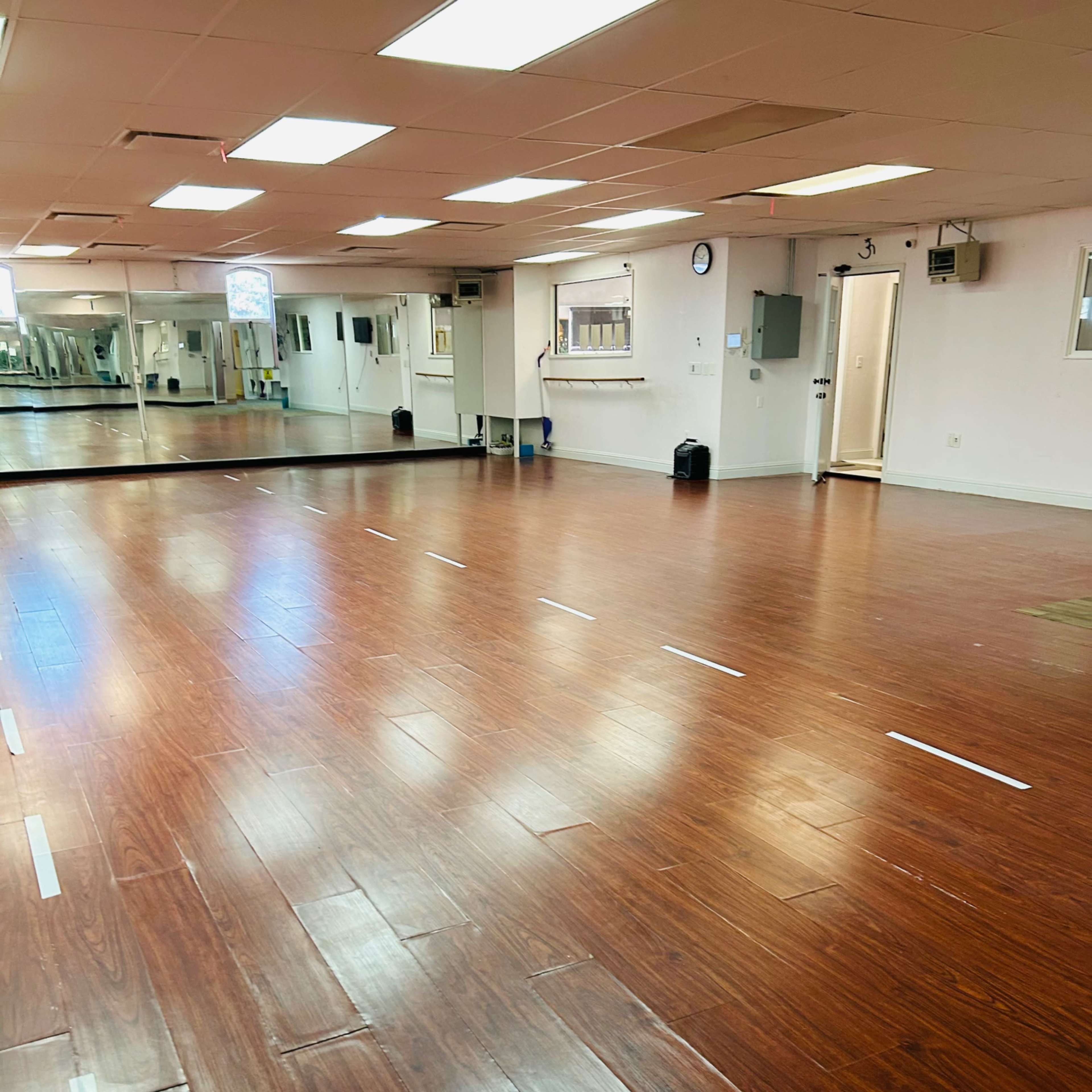 A spacious dance studio with a polished wooden floor and large mirrors along one wall.