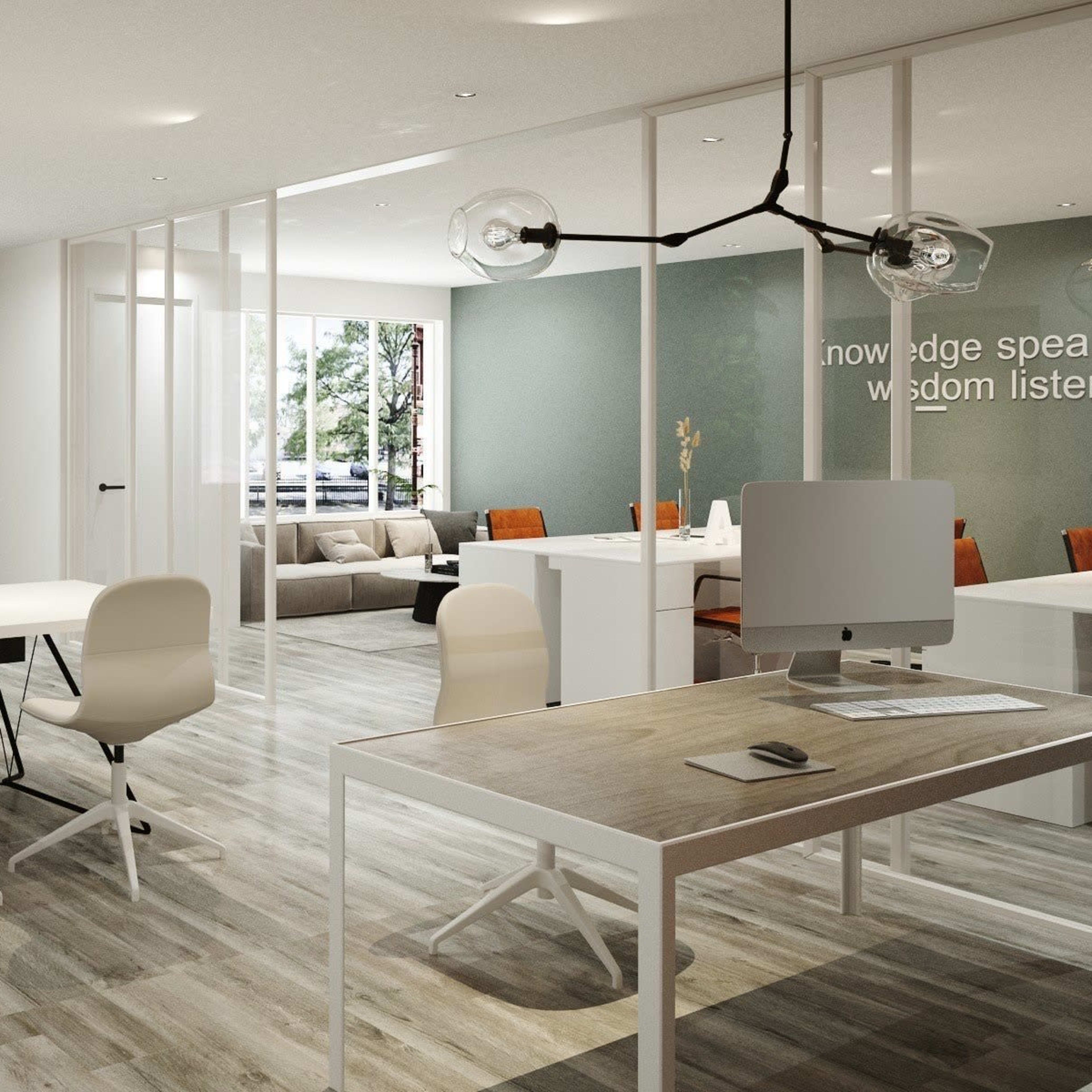 A modern office space featuring a large collaborative table, individual workstations, and a seating area with a sofa, all surrounded by windows allowing natural light to enter.