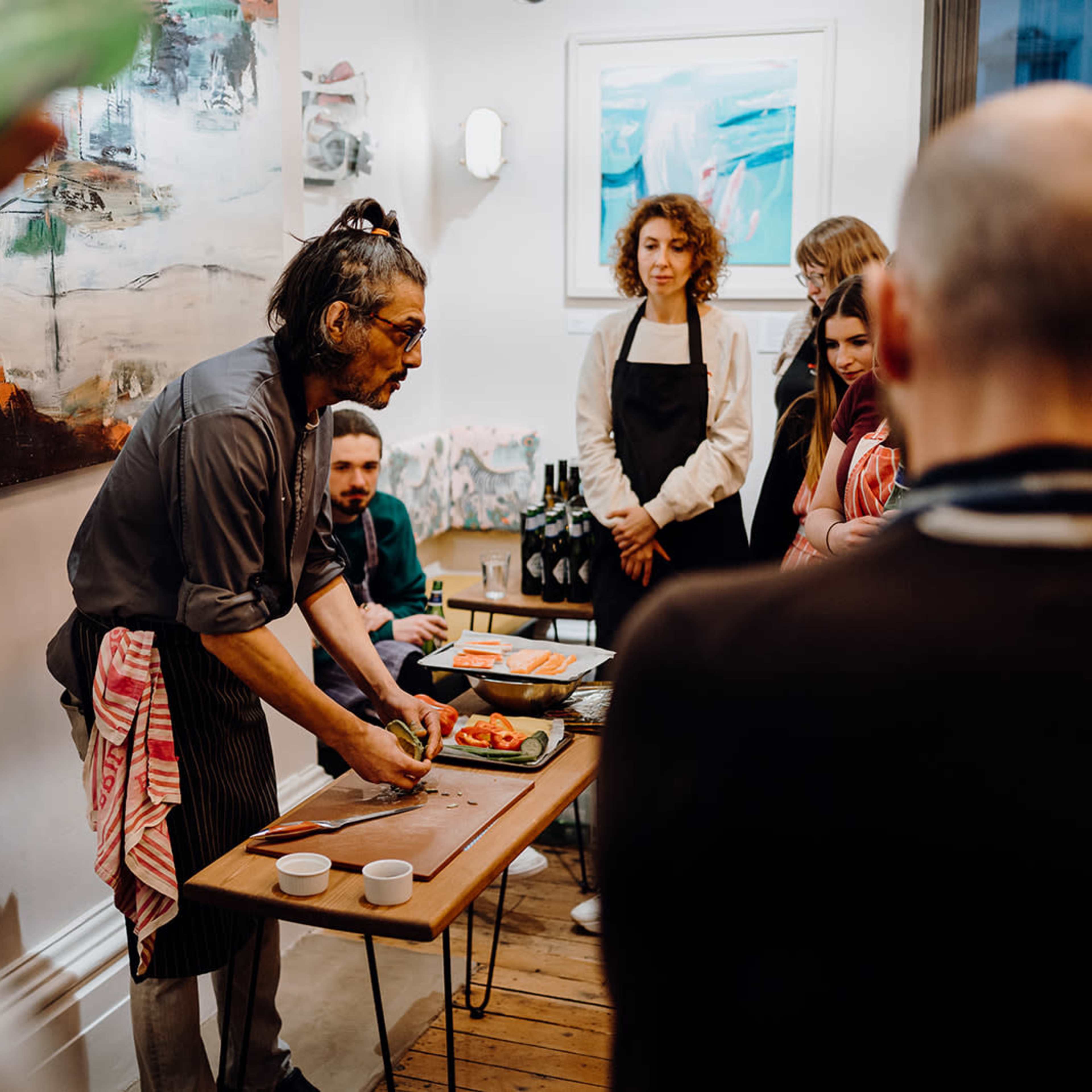 A chef demonstrates food preparation techniques to an attentive audience in a vibrant kitchen setting.