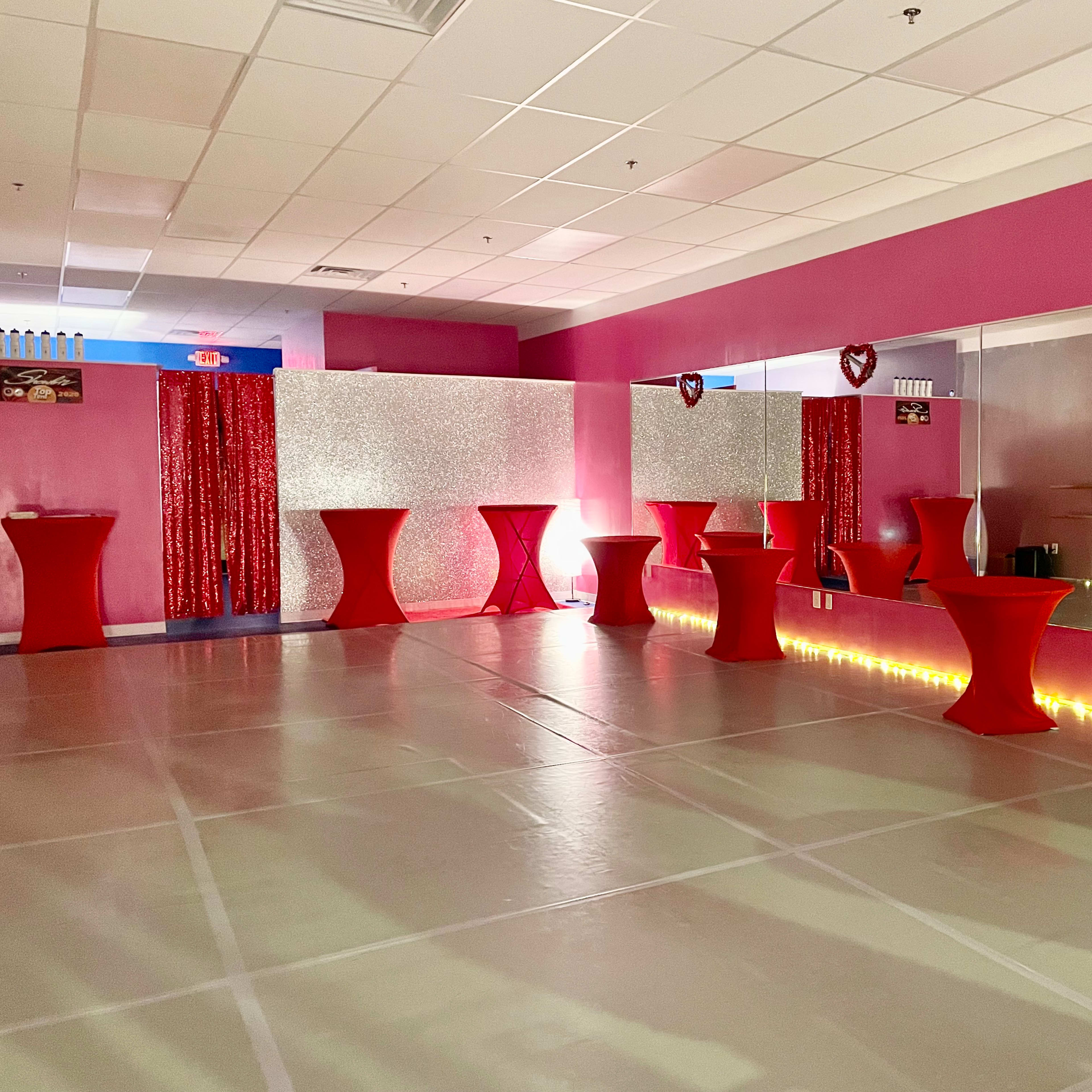 An event space featuring red tablecloth-covered tables, pink walls, and decorative lighting along the floor.
