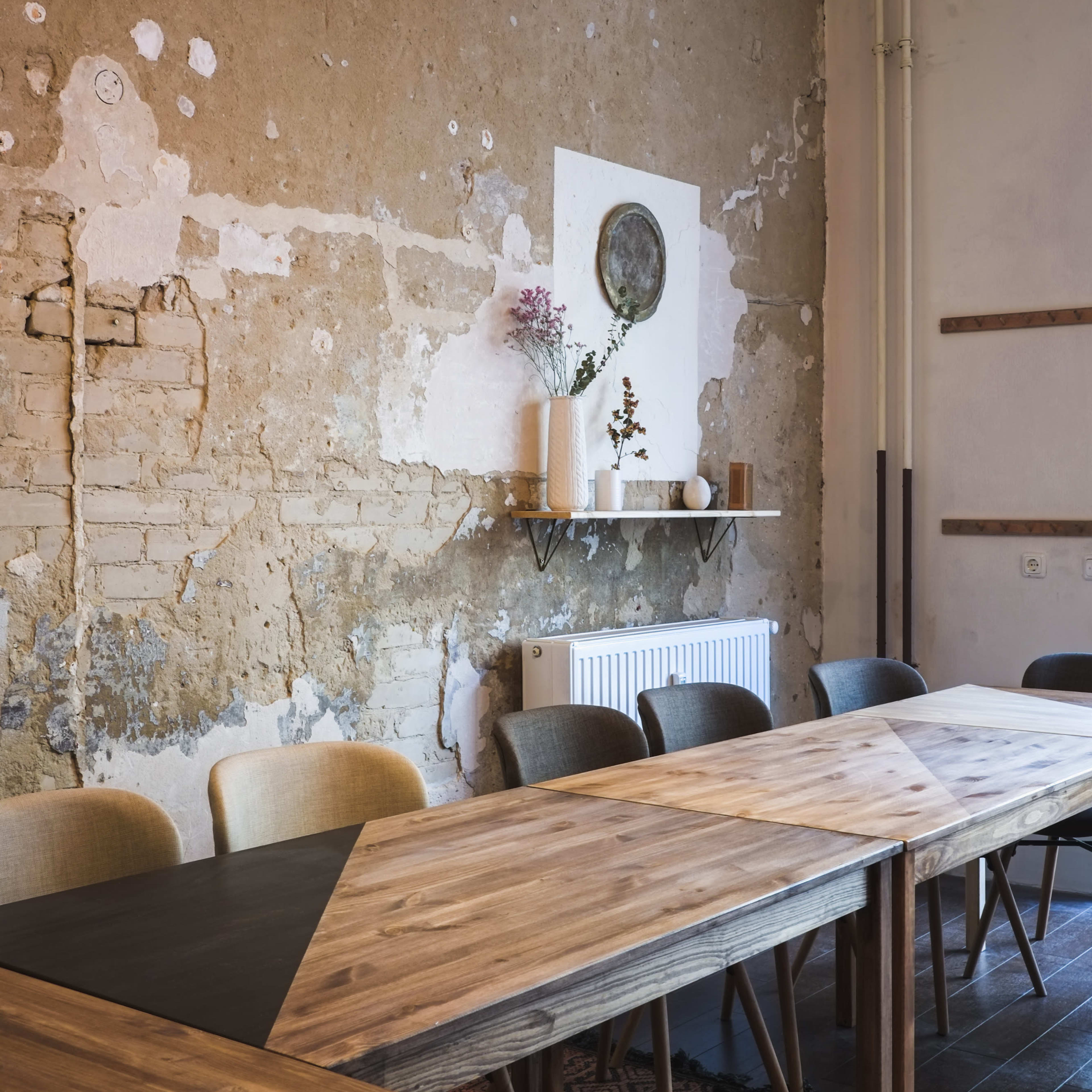A wooden dining table is set in a room with peeling walls, featuring a pendant light and decorative items on a shelf.