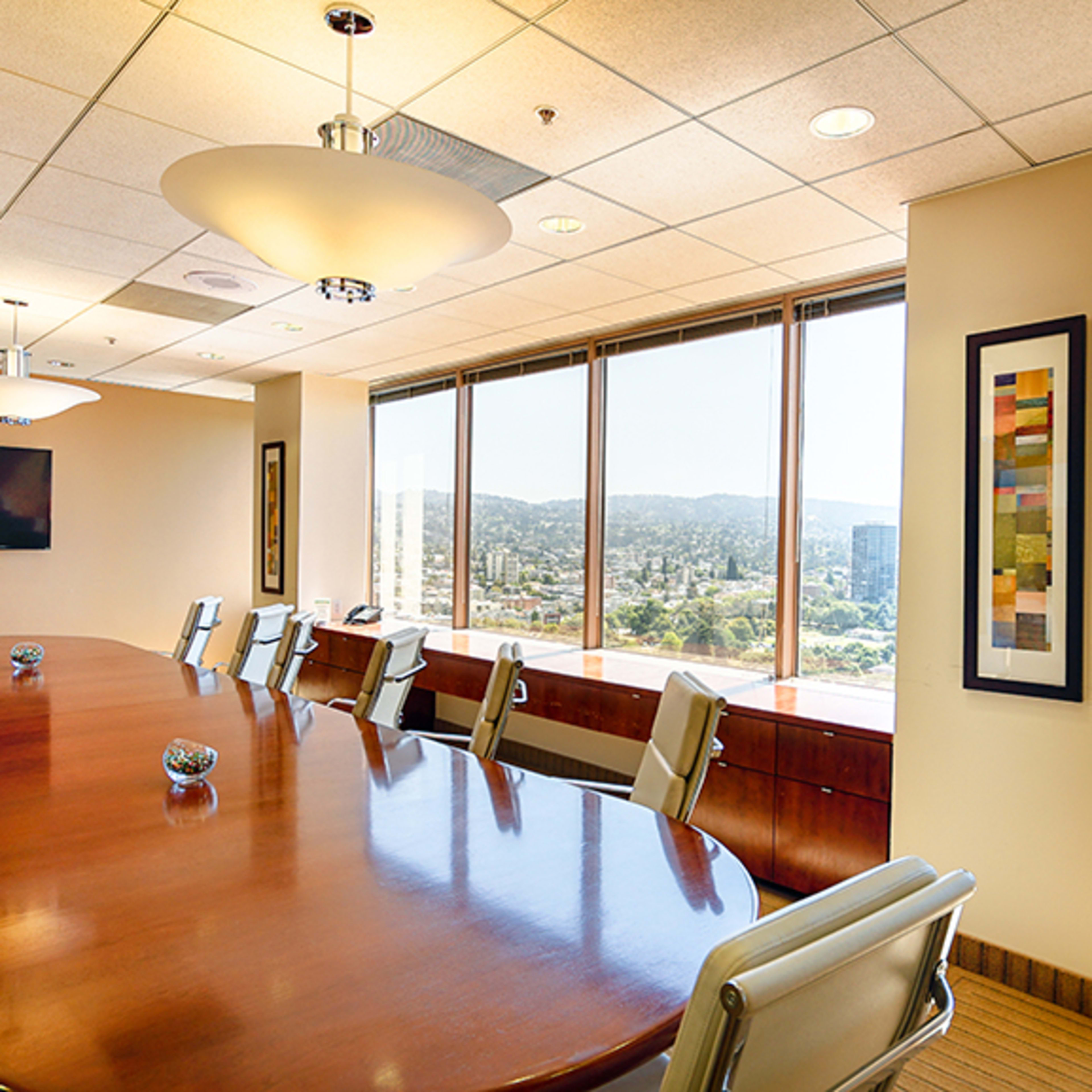A large conference room features a wooden table surrounded by white chairs, with large windows offering a view of the cityscape.