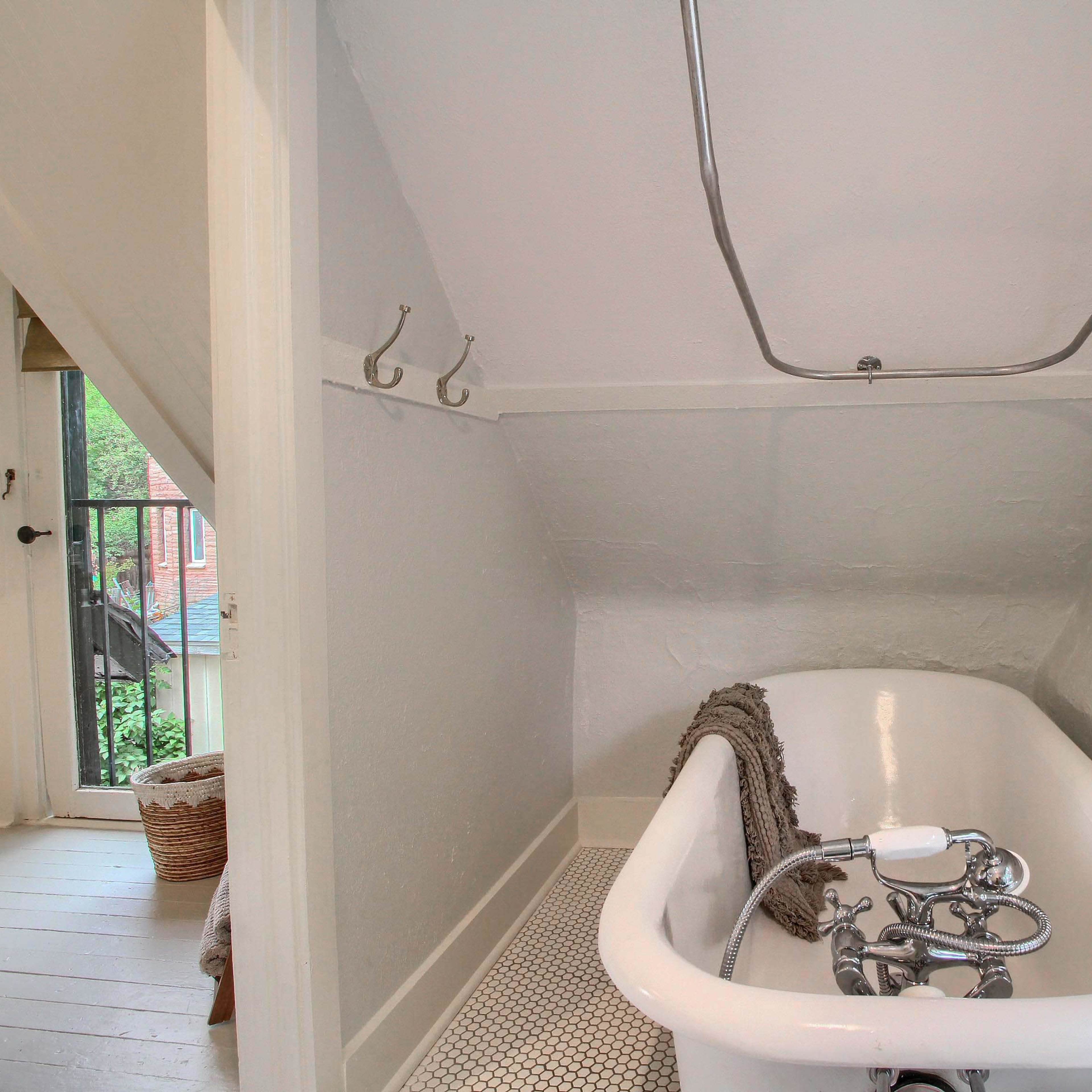 A white clawfoot bathtub is positioned against a light gray wall in a small, sloped bathroom.
