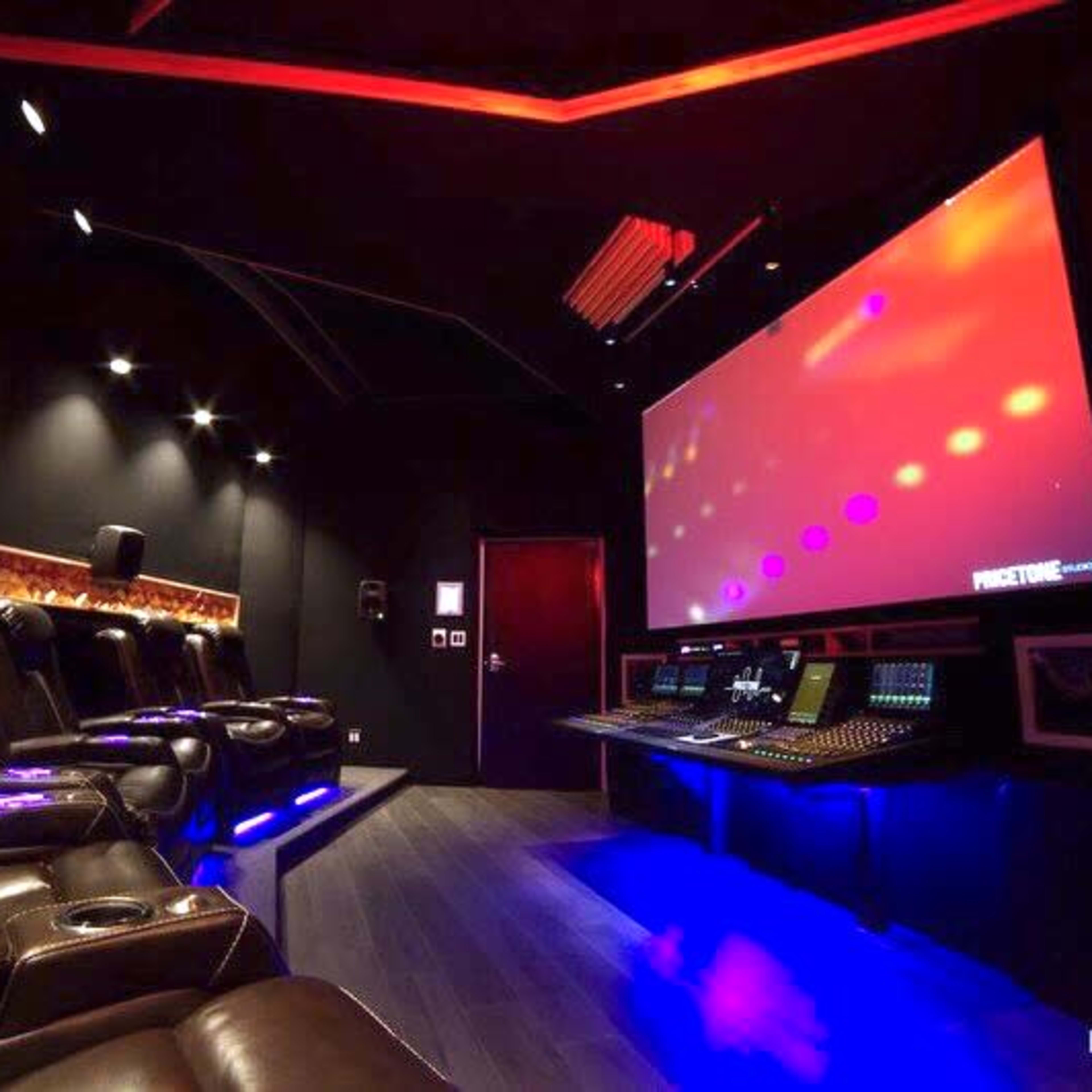 A modern home theater features dark upholstery seating, a large projection screen, and a sound mixing console.
