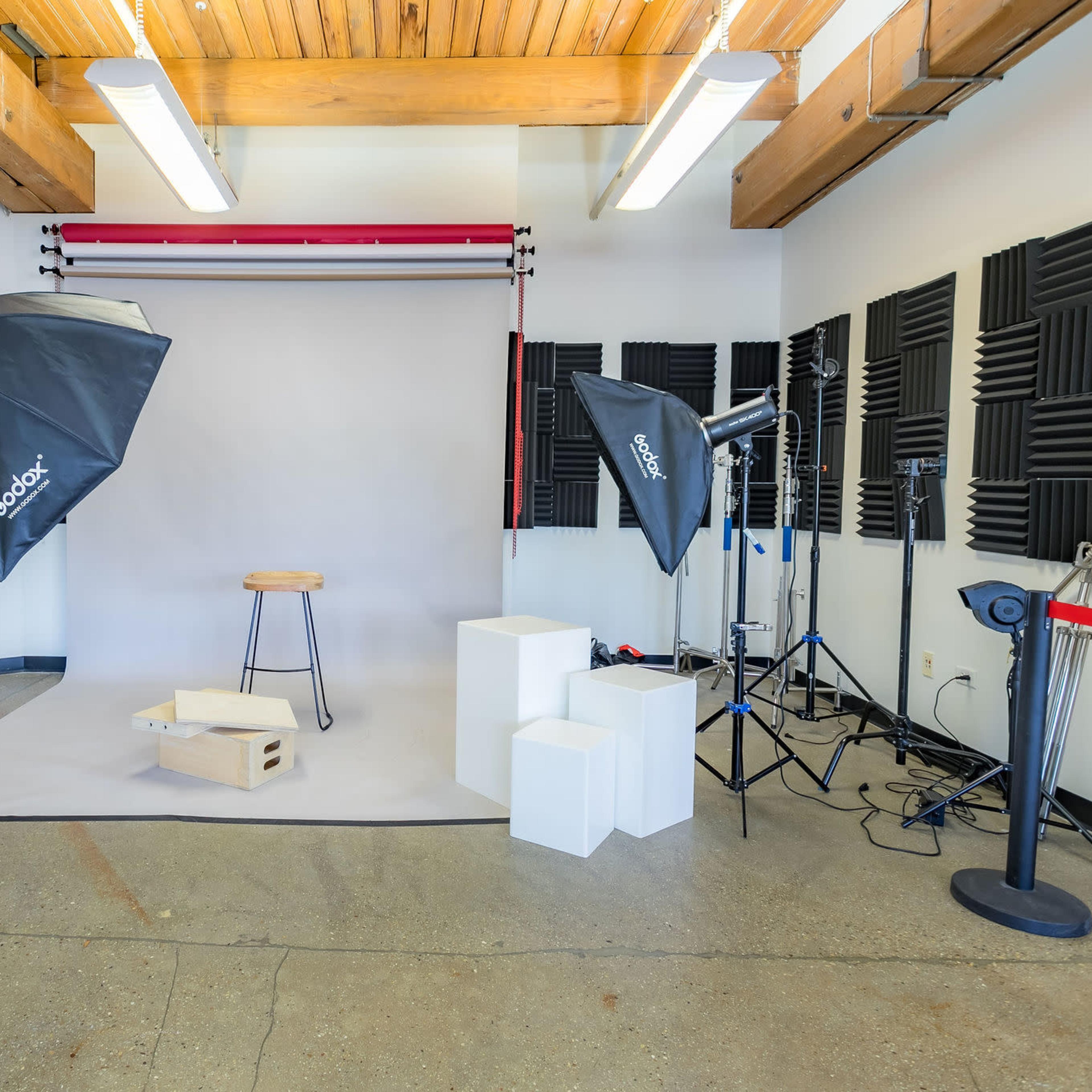A photography studio setup with lighting equipment, softboxes, and a backdrop featuring a stool and white blocks.