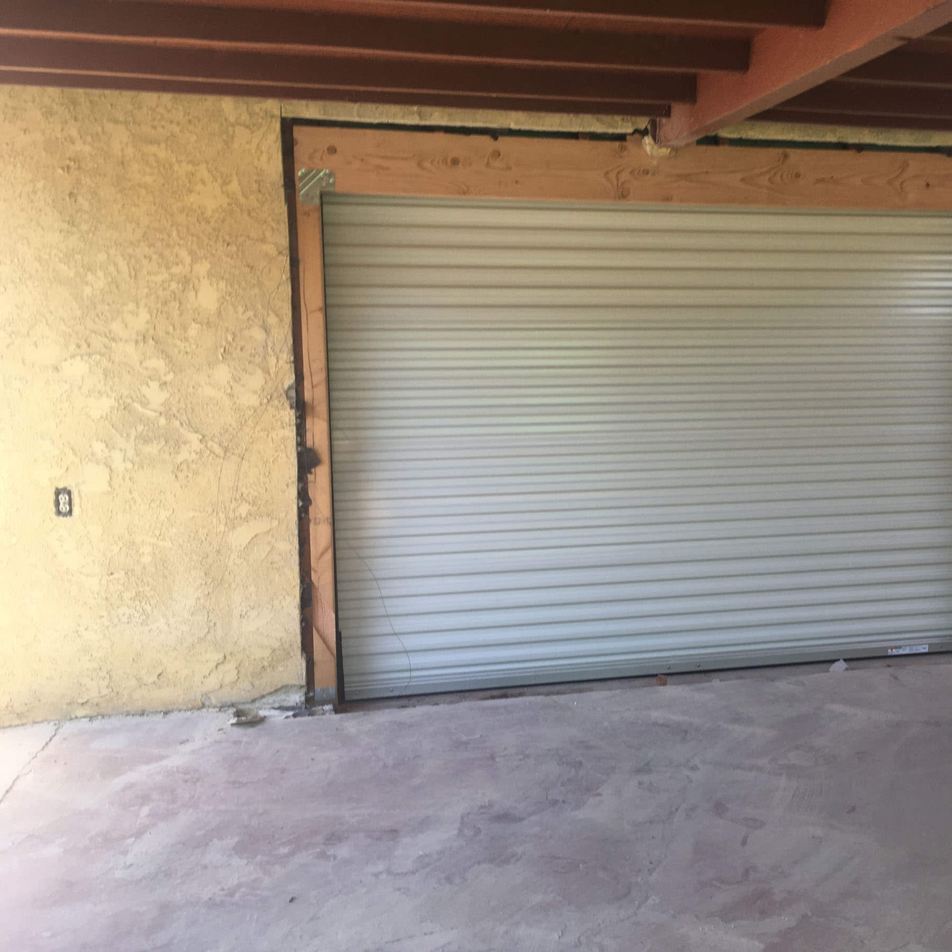 A partially constructed opening for a roll-up garage door with a metal door partially installed in a stucco wall.