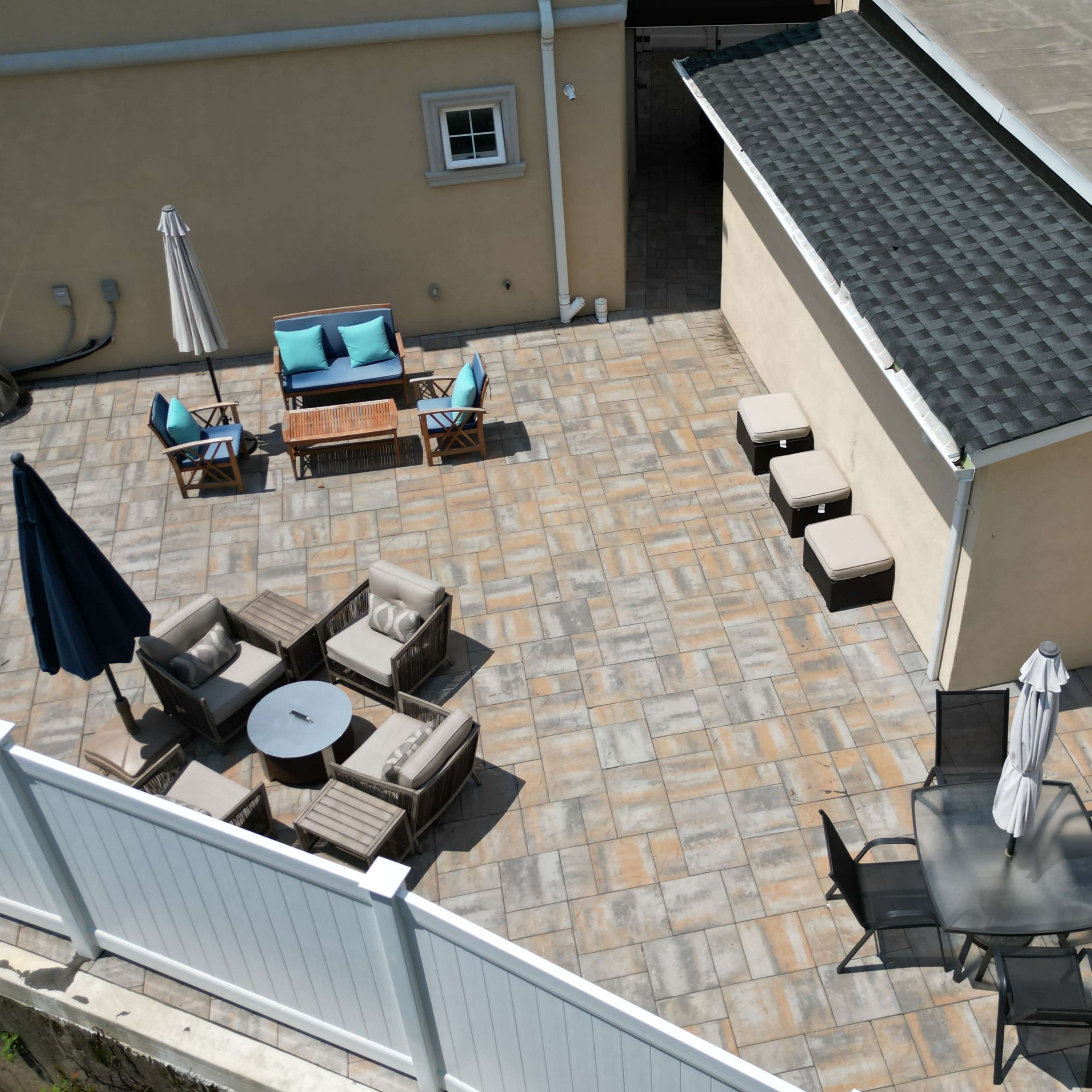 A patio area featuring several seating arrangements, including lounge chairs, a table with chairs, and a shaded umbrella.