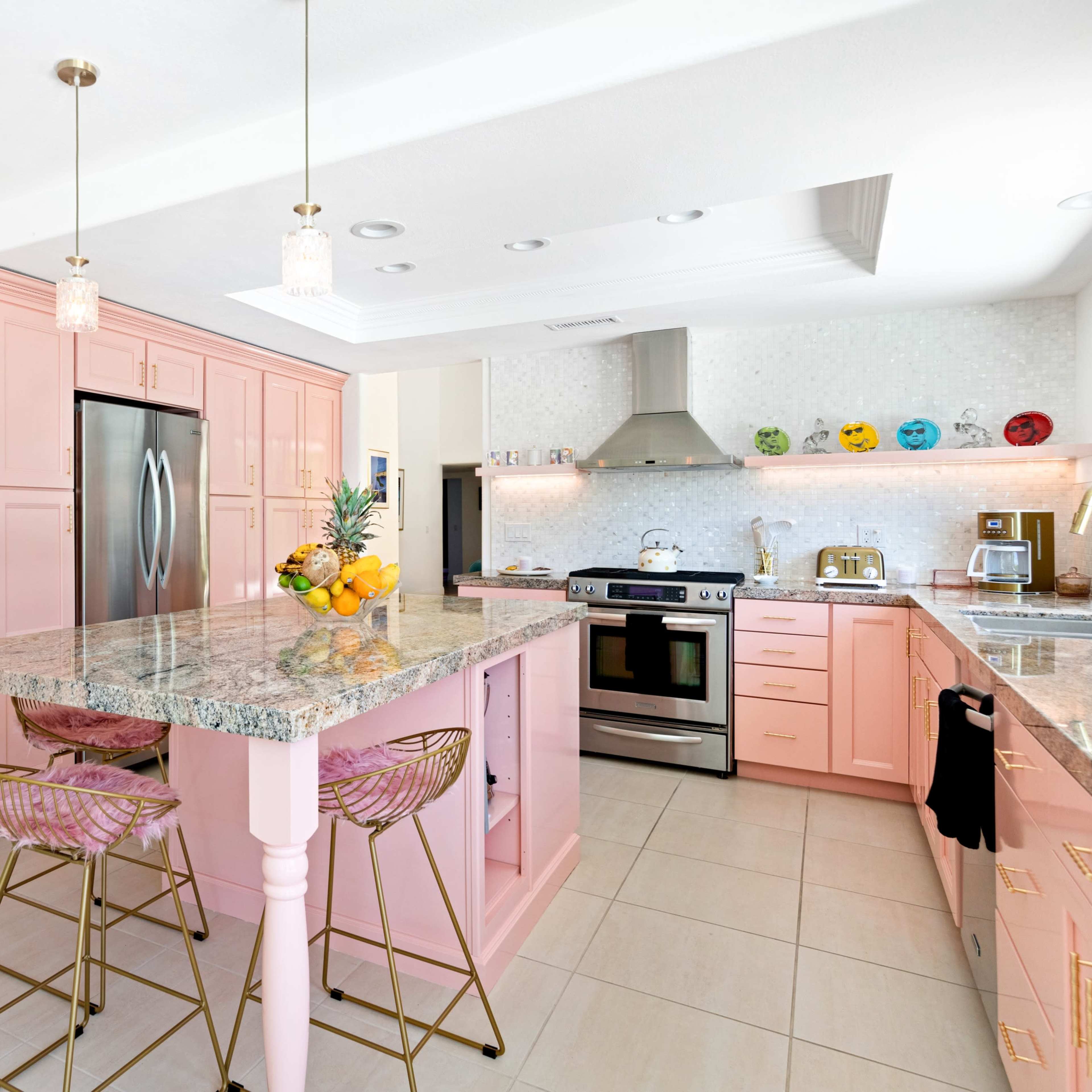 The kitchen features pink cabinetry, a granite island with bar stools, and stainless steel appliances.