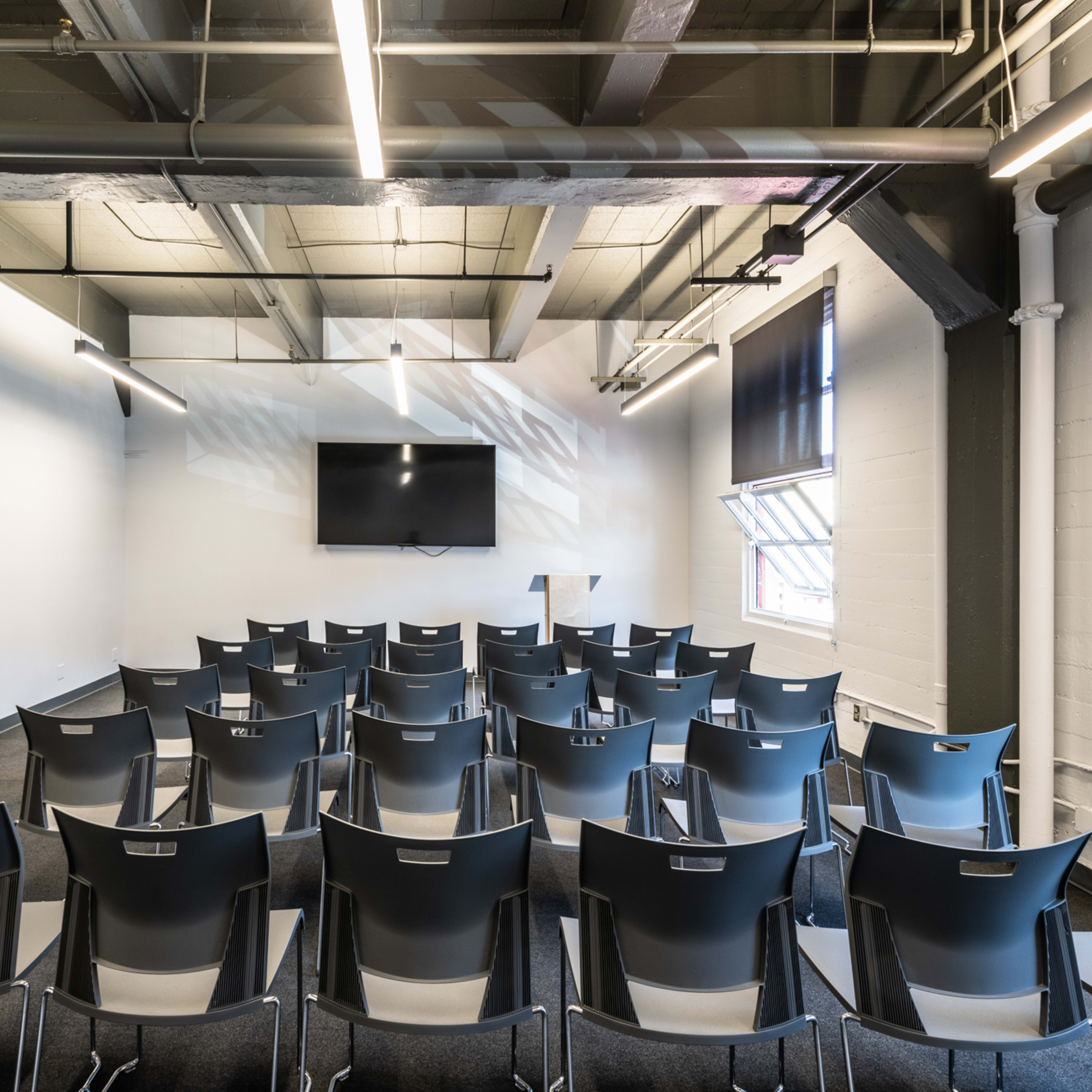 A meeting room features rows of metal chairs facing a wall-mounted television.