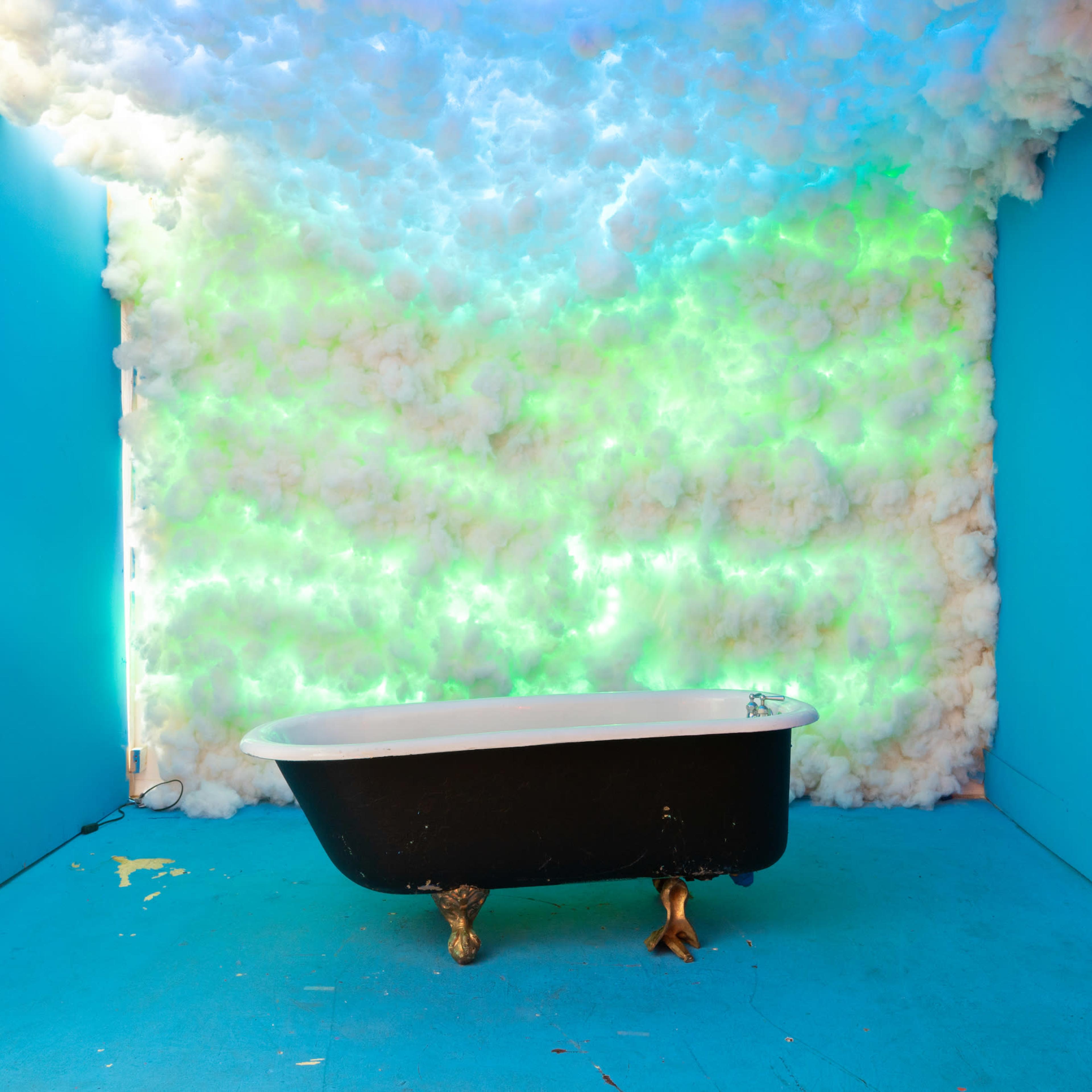 A vintage black and white bathtub positioned in a room with bright blue walls and a cloud-like, colorful backdrop.