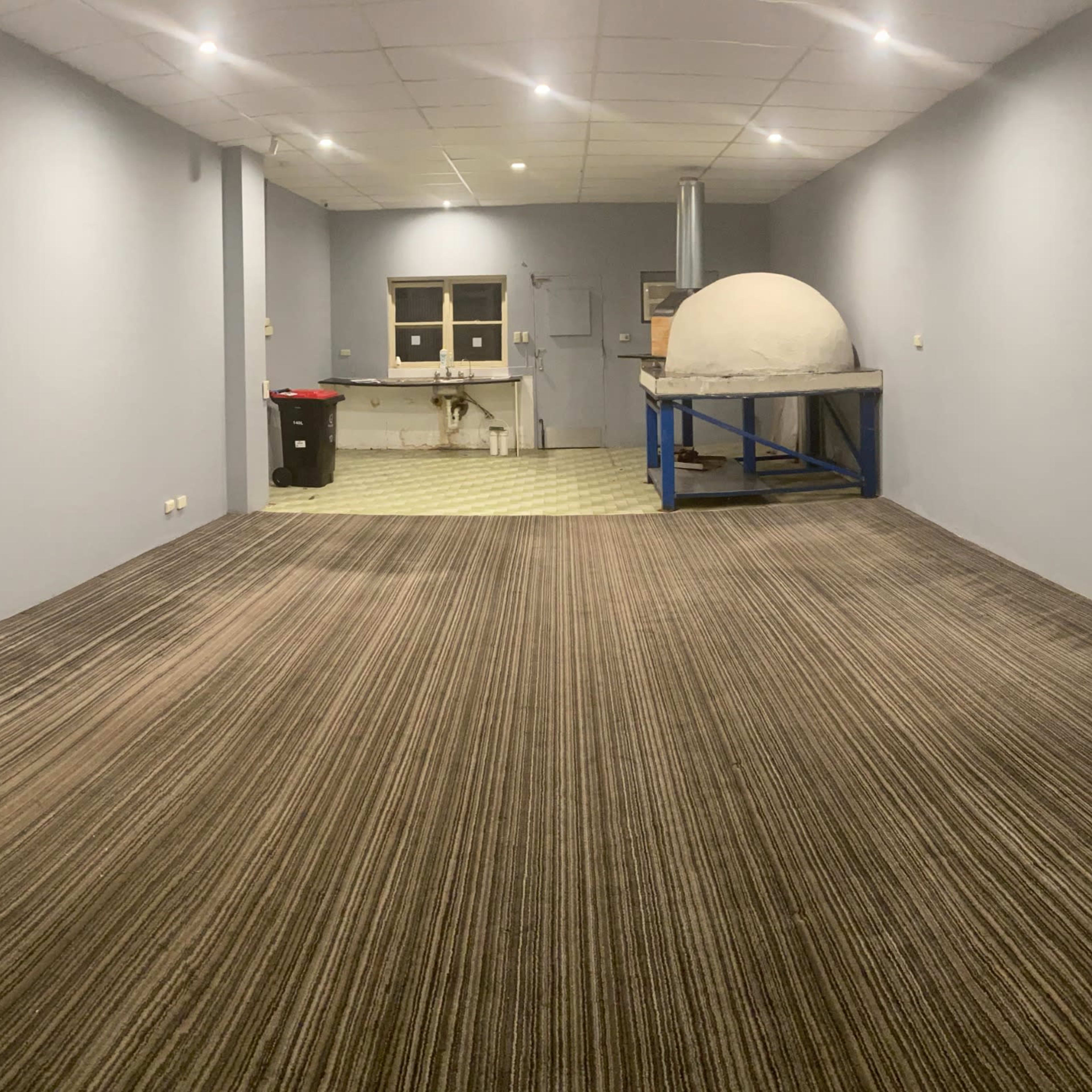 A wide, empty room with gray walls, a patterned carpet, and a round structure on a blue table at the far end.