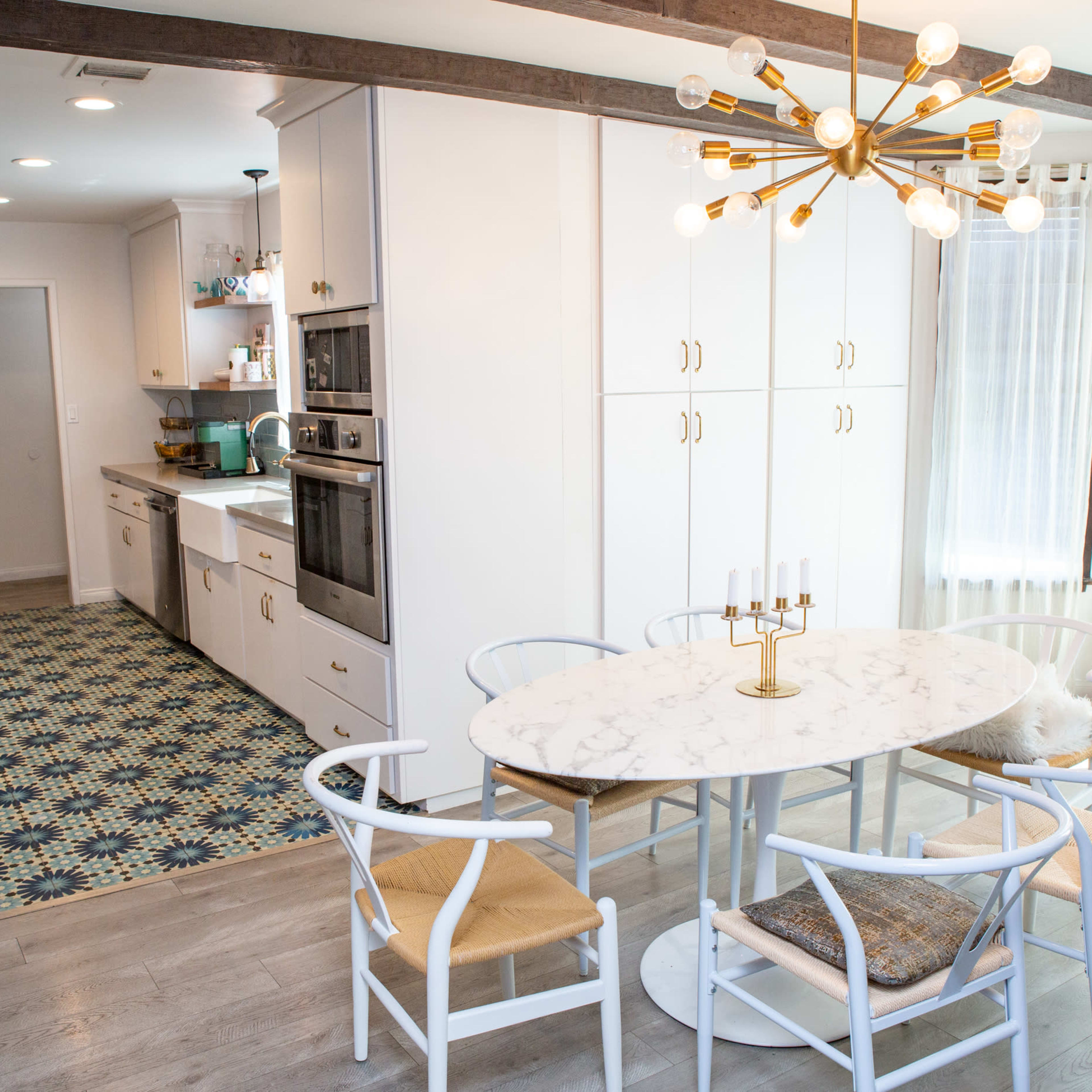 A modern kitchen and dining area featuring an oval marble table surrounded by white chairs, with cabinetry and appliances in a light color scheme.