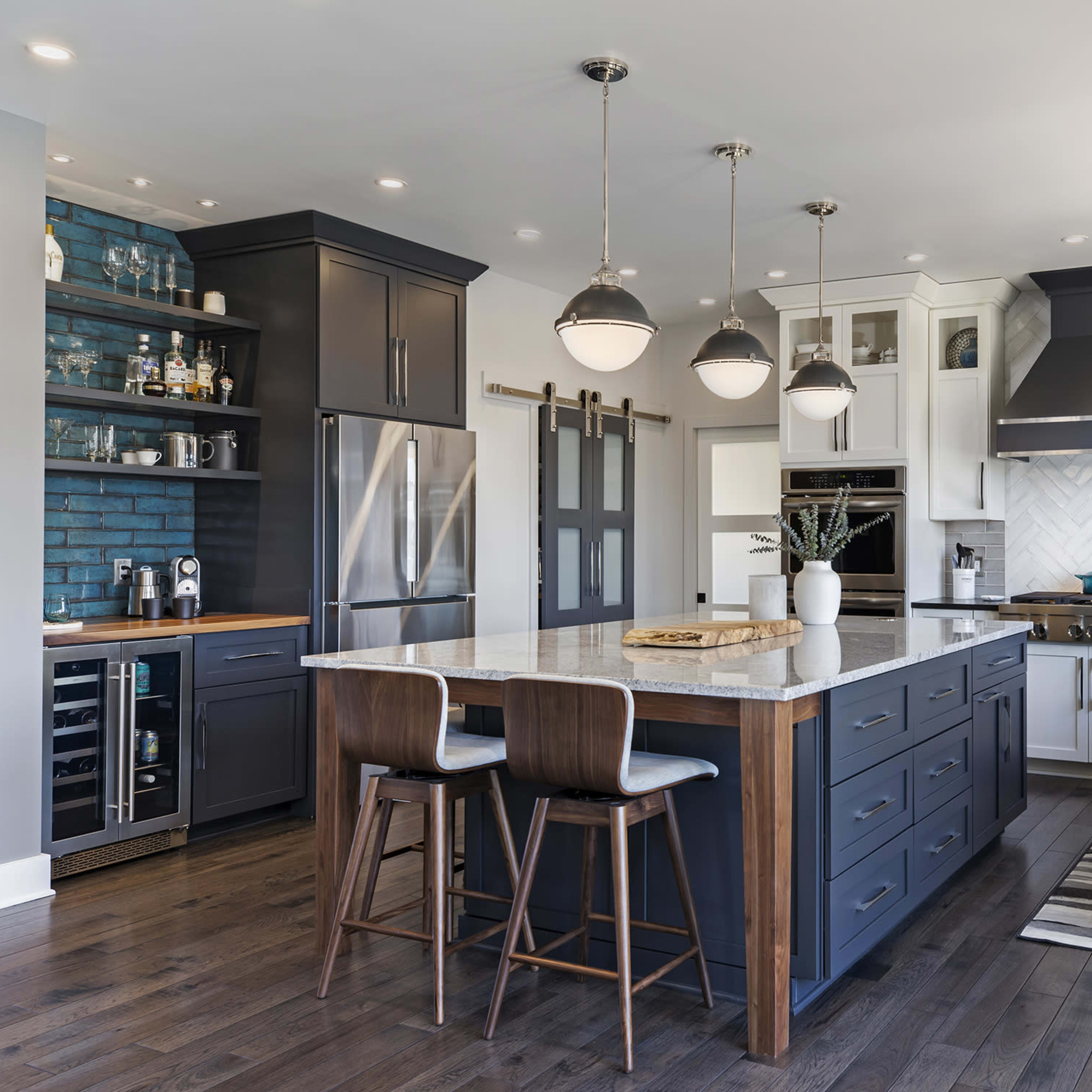 A modern kitchen featuring a central island with seating, dark cabinetry, stainless steel appliances, and a mix of blue and white accents.