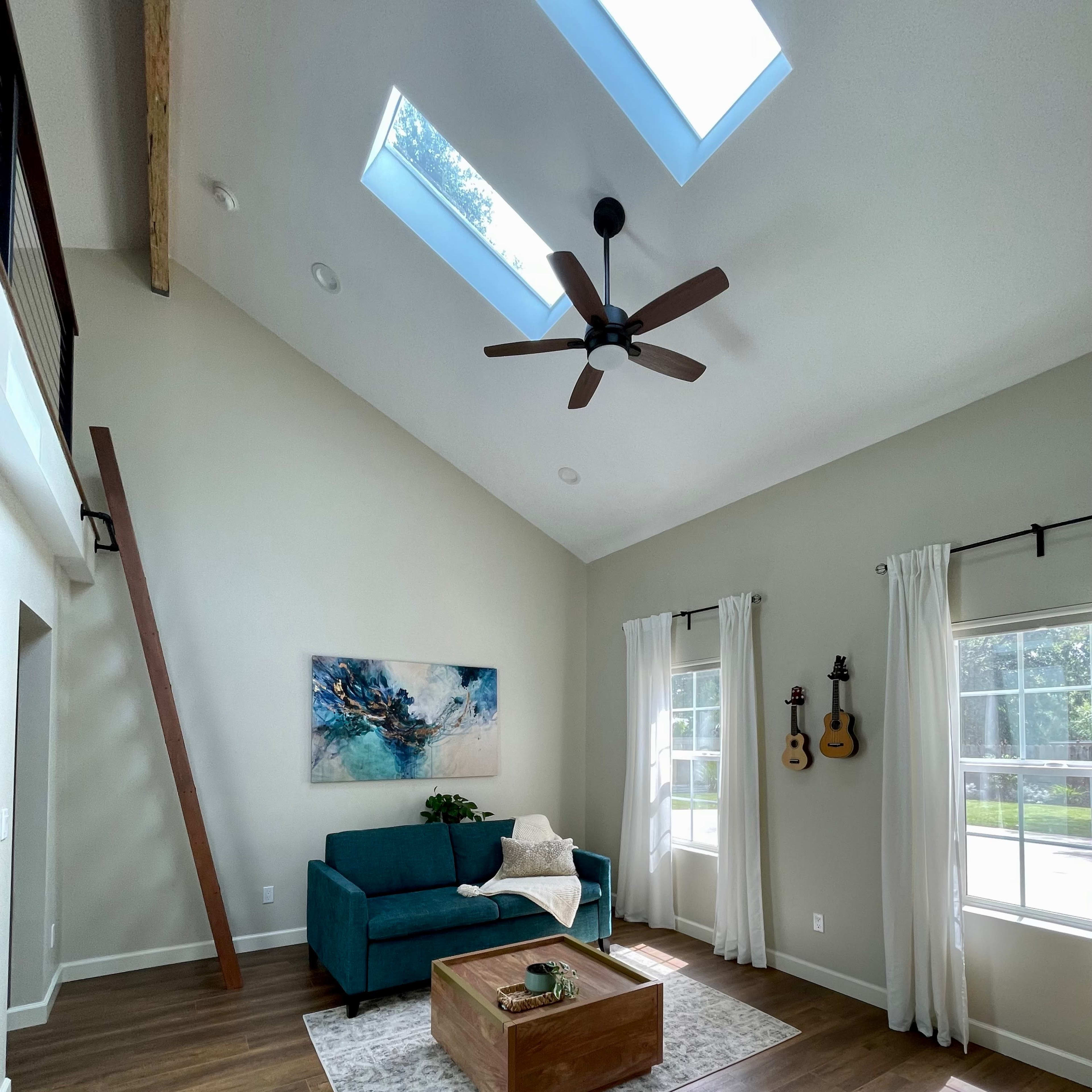 A bright, airy living room features a teal sofa, a wooden coffee table, and two guitars hanging on the wall under skylights.