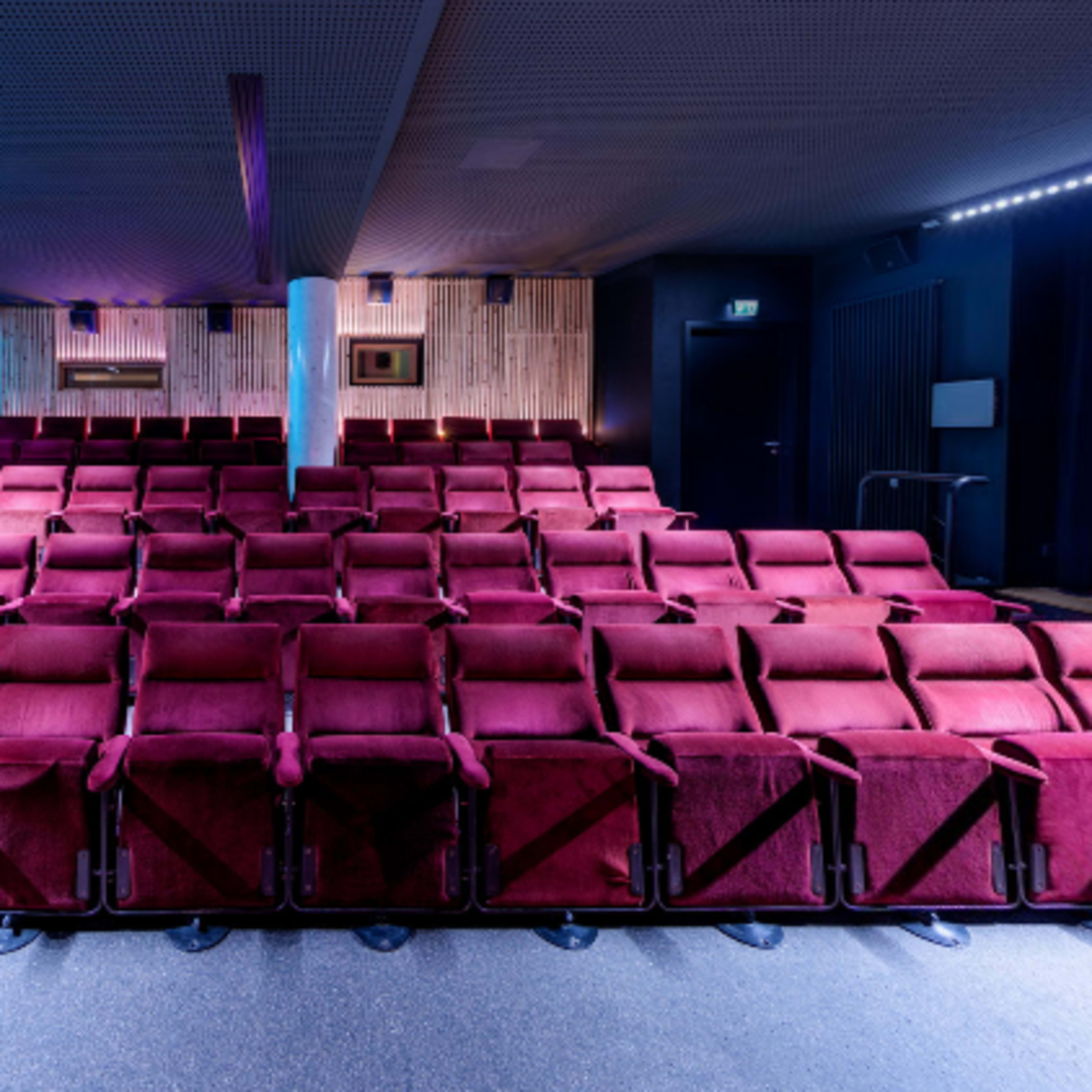 A row of red upholstered theater seats arranged in a dimly lit auditorium.