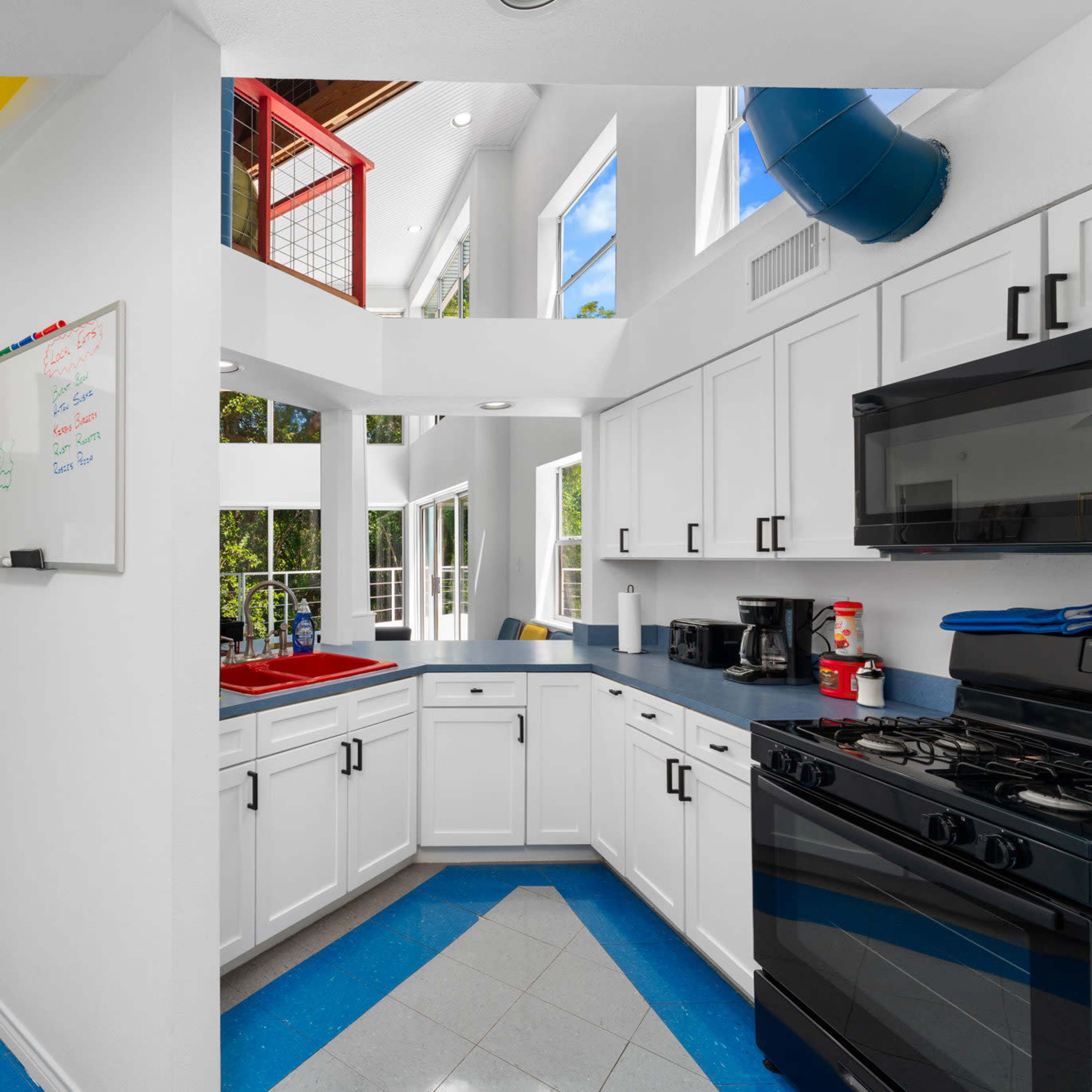 A modern kitchen with white cabinetry, a dark countertop, and large windows that provide natural light.