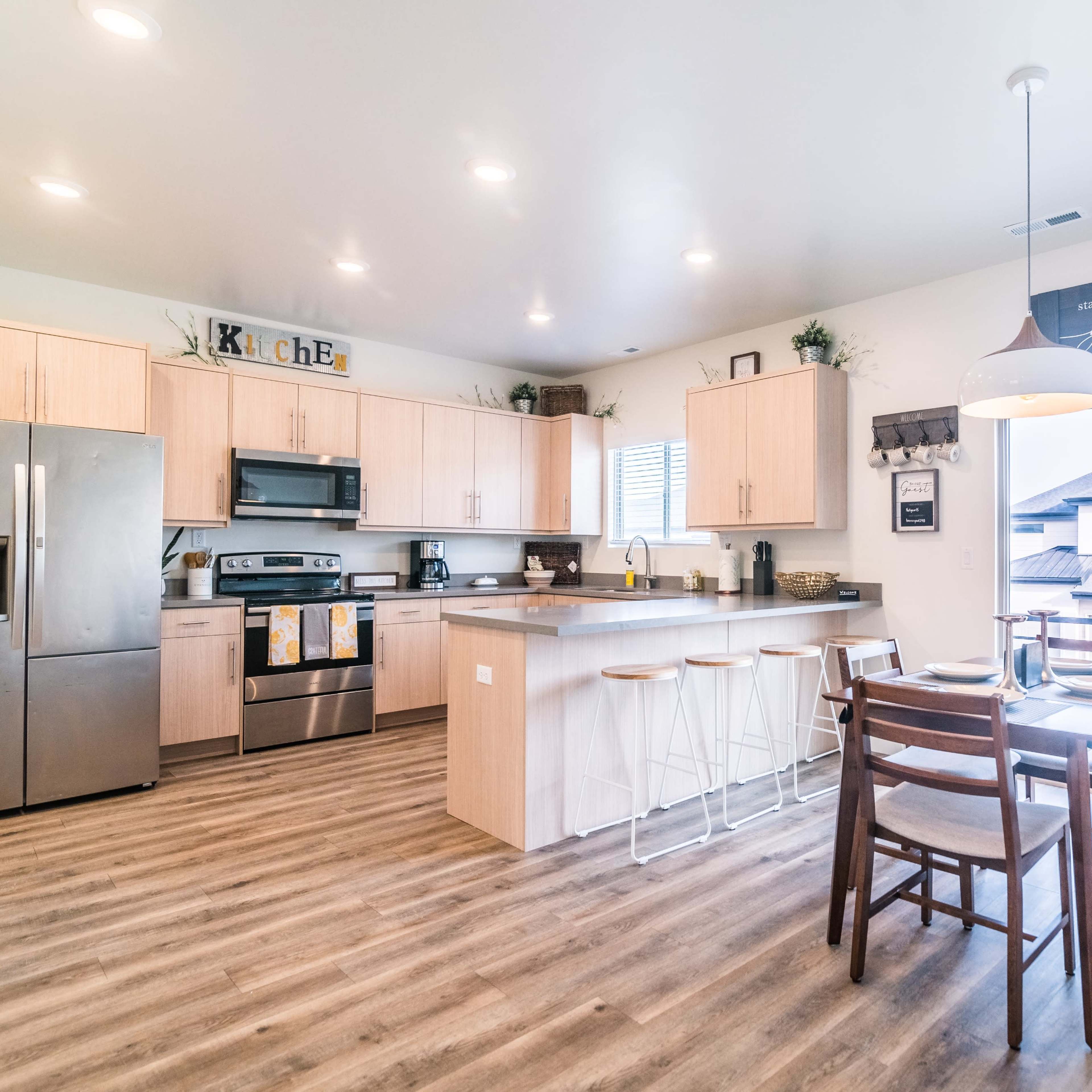 A modern kitchen features wooden cabinetry, stainless steel appliances, and a dining area with a table and chairs.