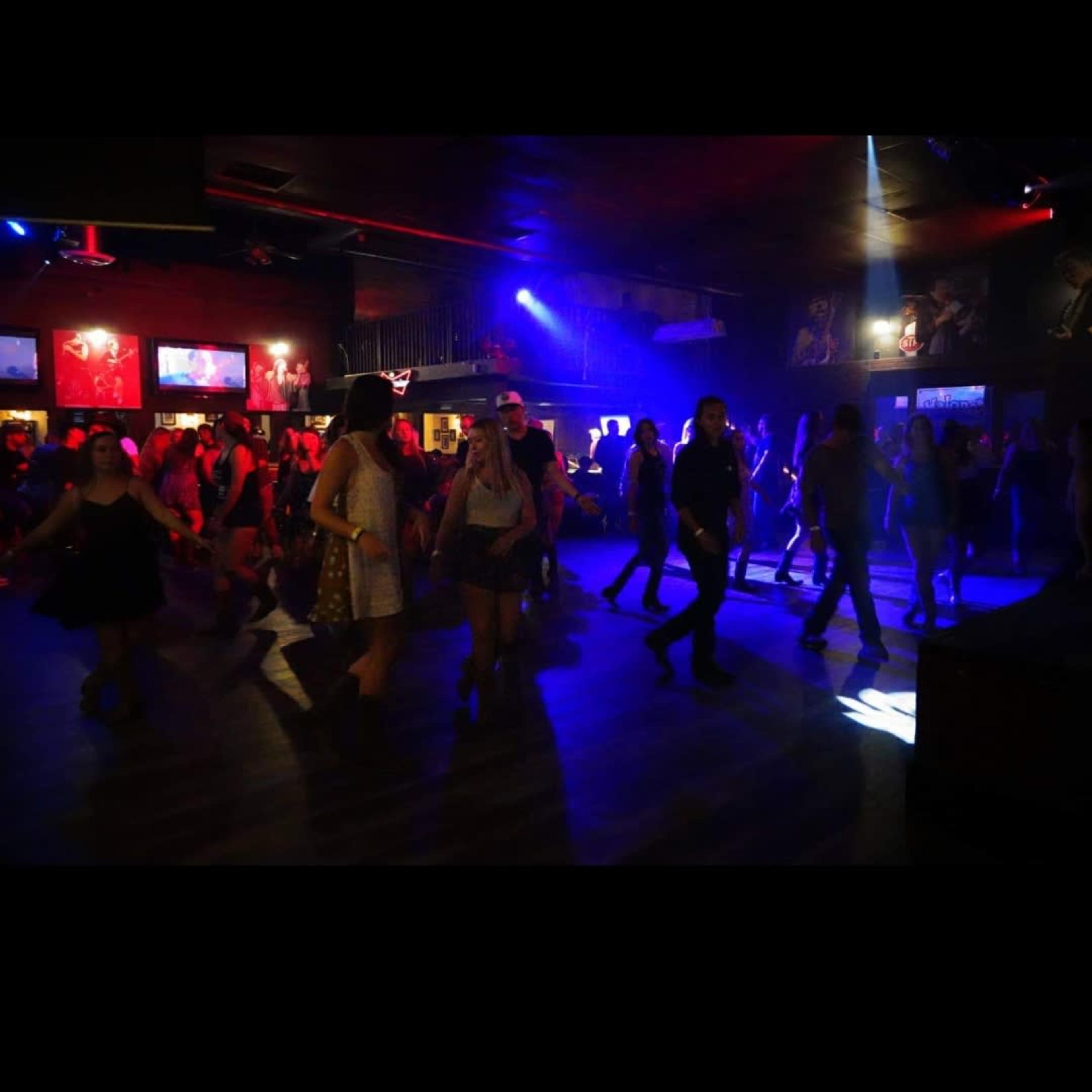 A crowd of people dances in a dimly lit venue filled with colorful lights.