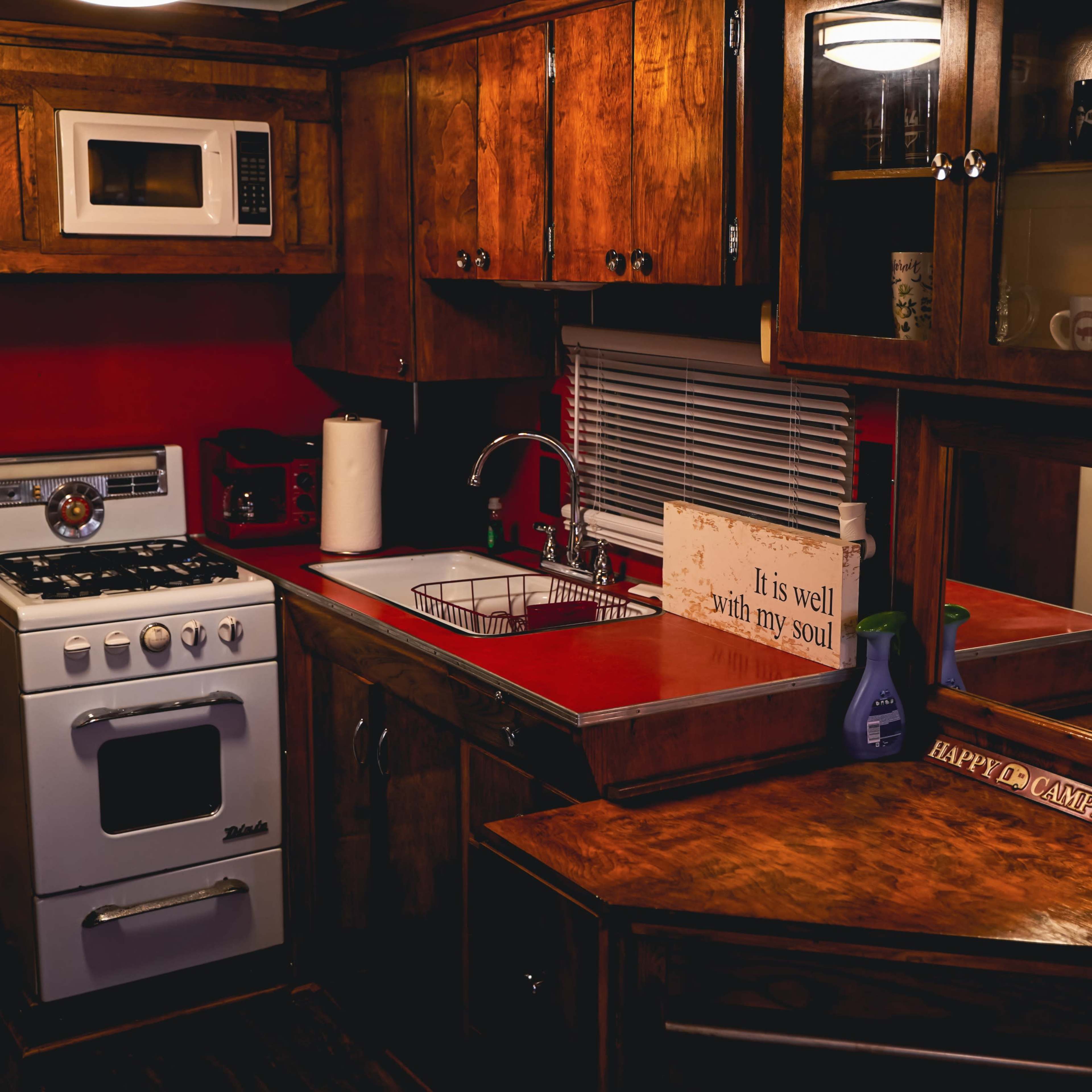 A compact kitchen with wooden cabinetry, a white gas stove, a microwave, a sink, and a red countertop.