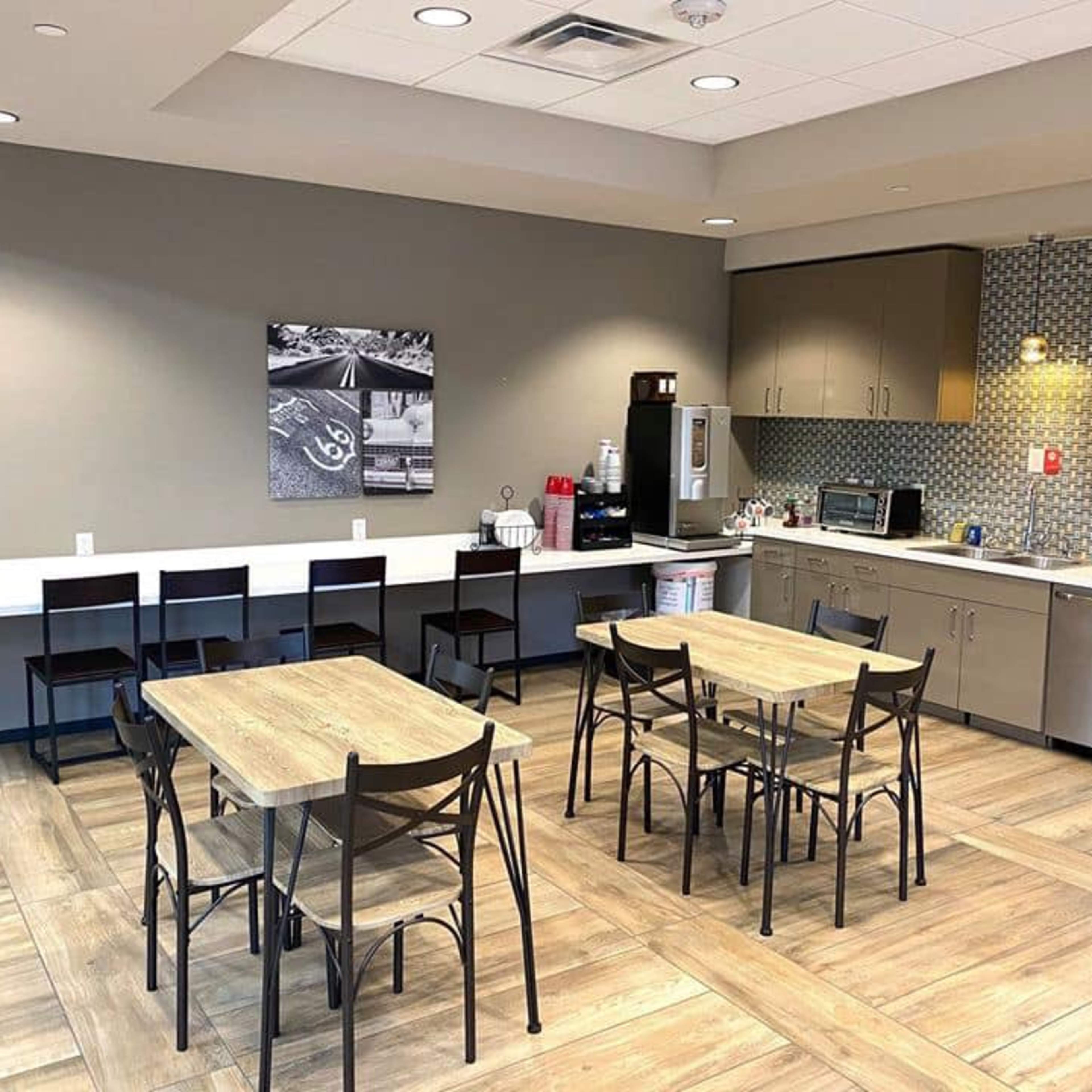 A modern kitchen area with two tables and chairs, a countertop with a coffee station, and various appliances along the wall.