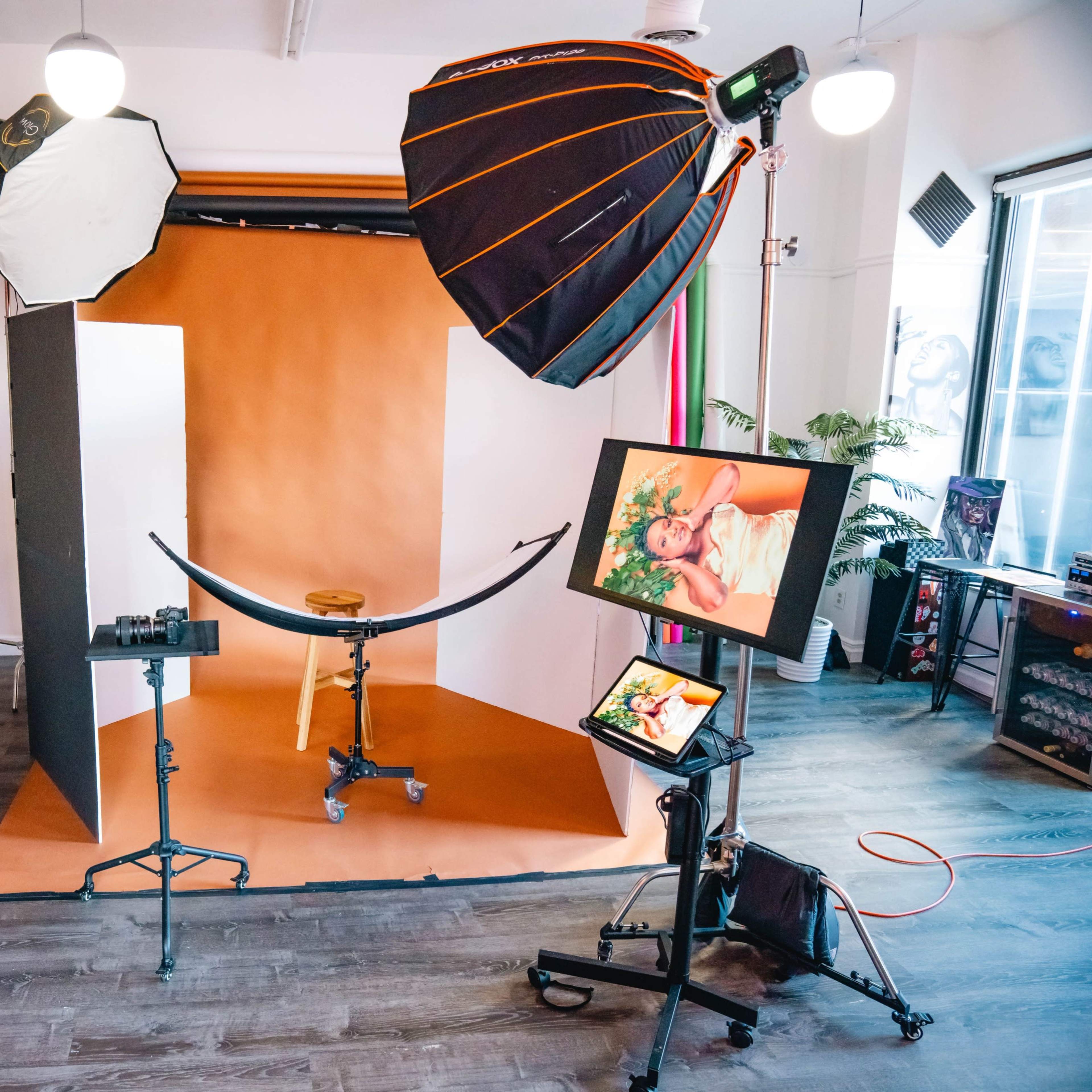 A photography studio setup with a backdrop, lighting equipment, a camera on a tripod, and a monitor displaying a photo.
