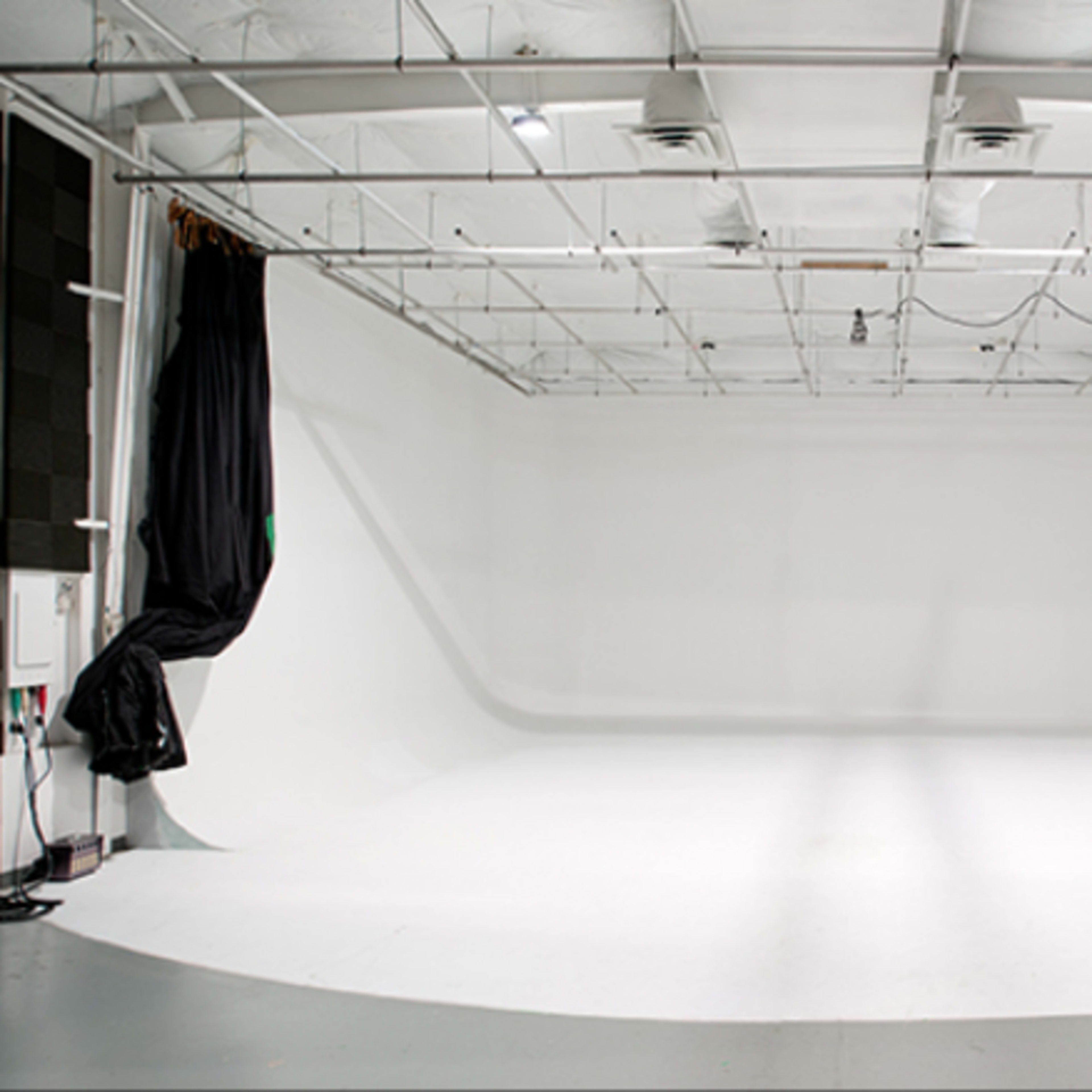 A spacious photo studio with a seamless white backdrop, high ceilings, and overhead lighting.