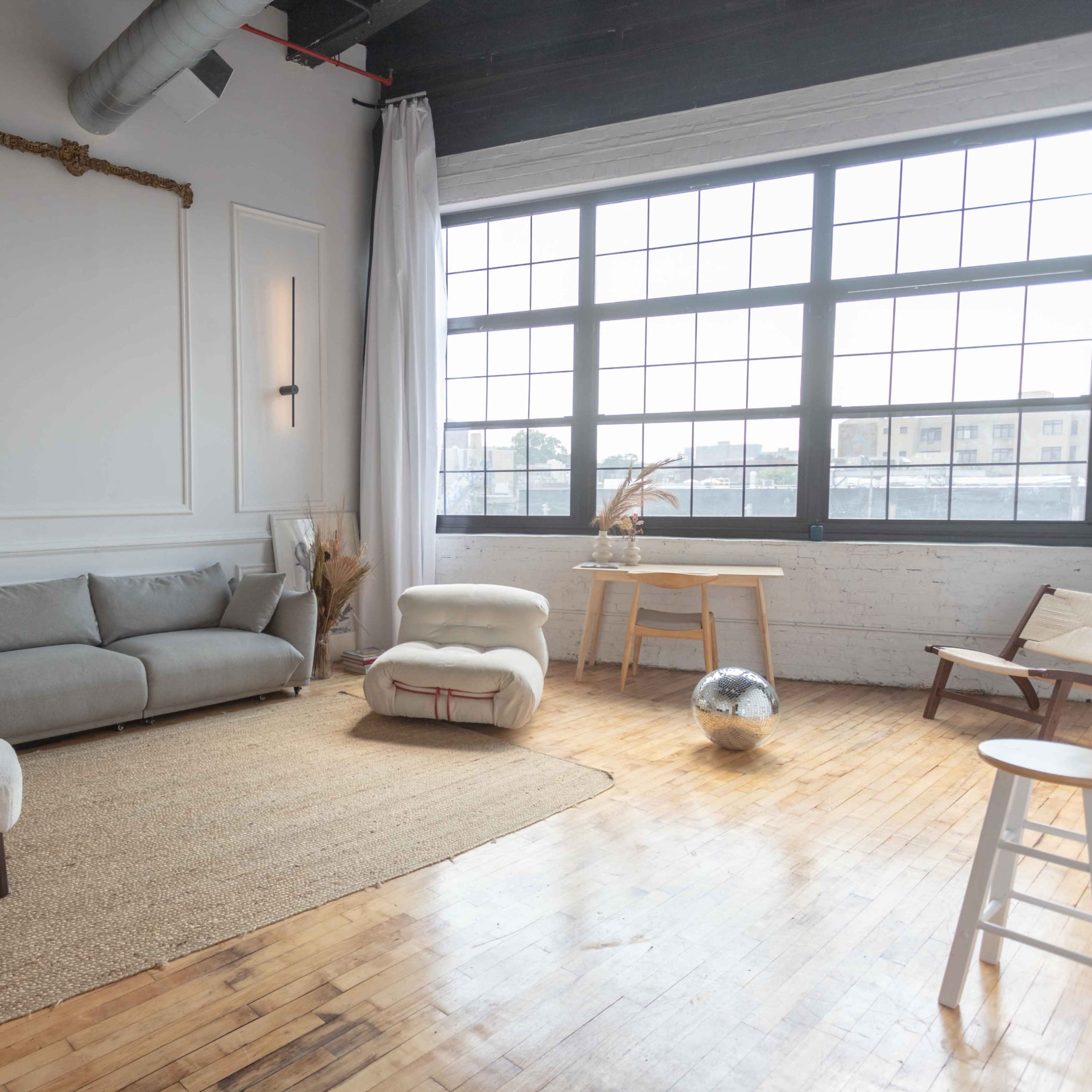 A spacious indoor area featuring a gray sofa, an upholstered chair, a round coffee table, and large windows that allow natural light to illuminate the wooden floor.