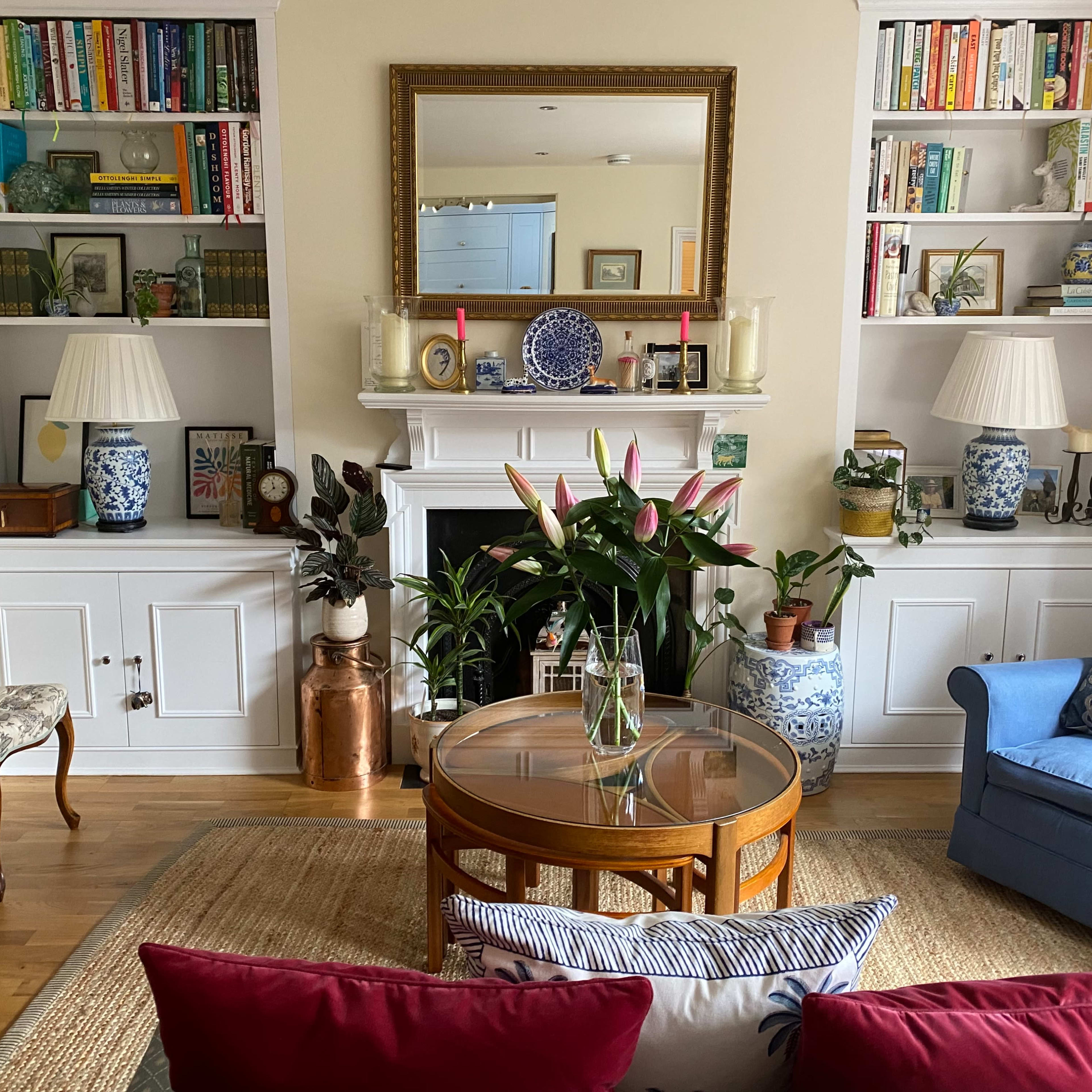 A cozy living room featuring a bookshelf filled with books, a fireplace with decorative items, and a coffee table surrounded by a sofa and chairs.