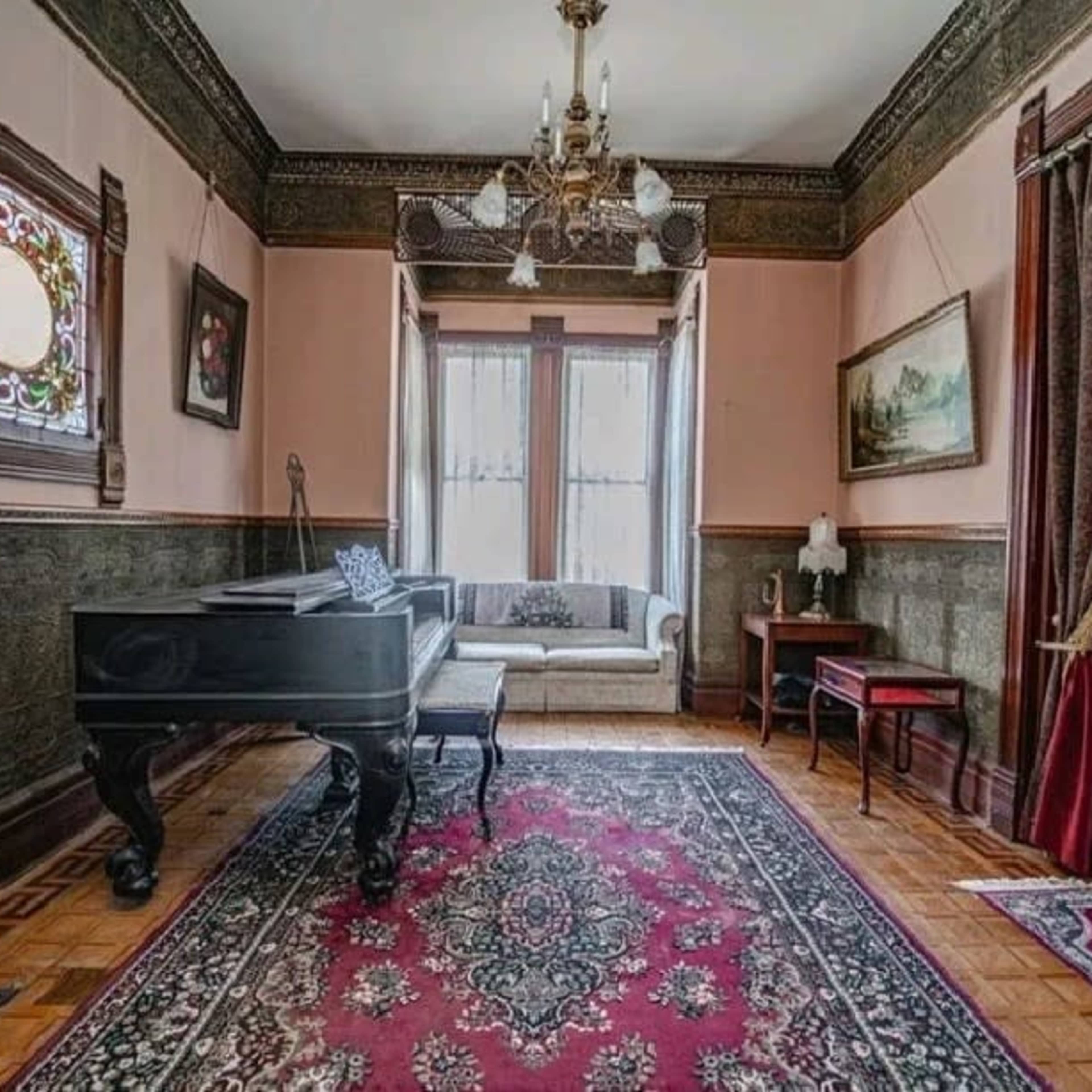 A vintage room featuring a grand piano, a patterned area rug, and ornate wall decorations, along with a couch and various furnishings.
