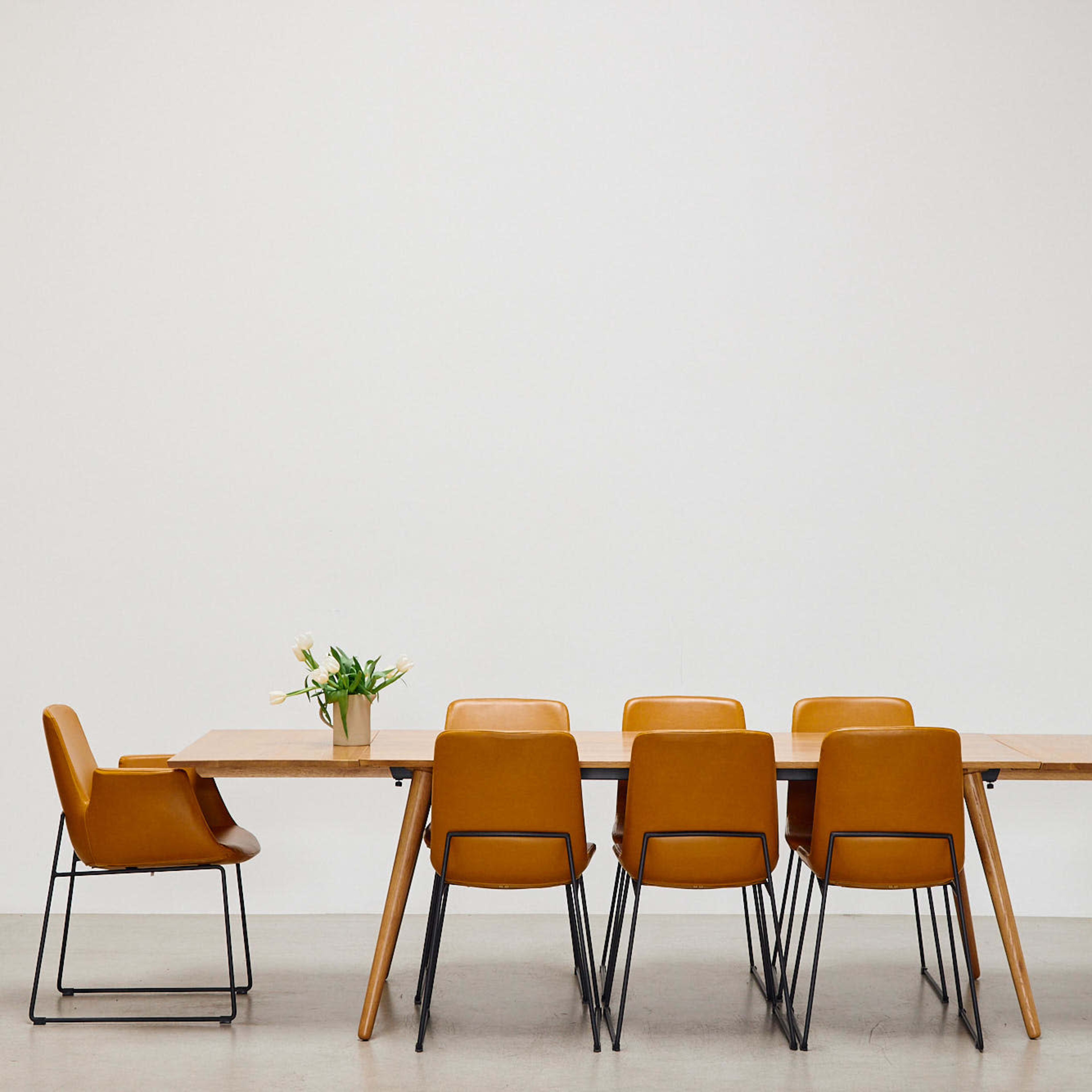 A wooden dining table with six yellow chairs is positioned against a plain white wall.