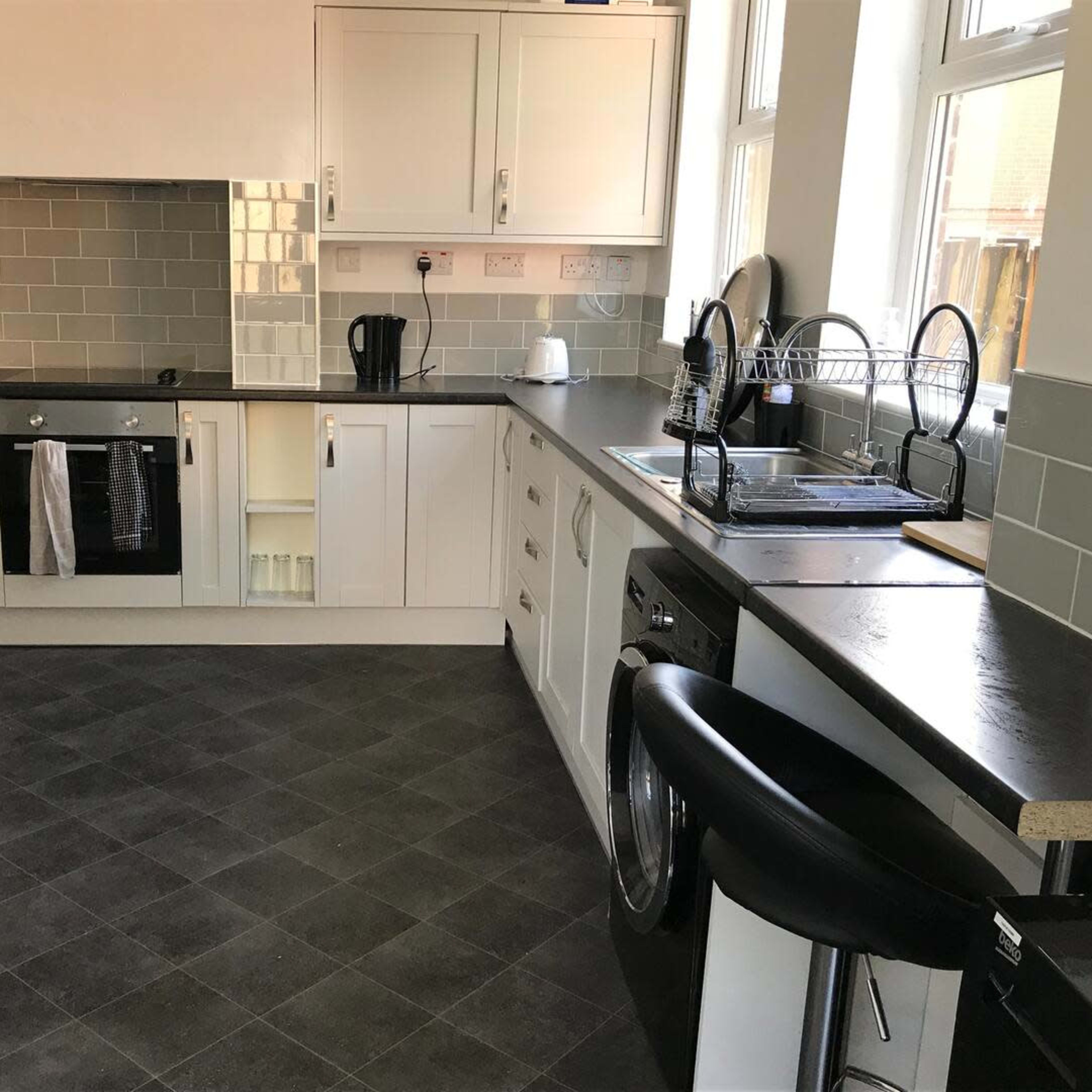 A modern kitchen with white cabinets, black countertops, and various appliances, including an oven and a washing machine.