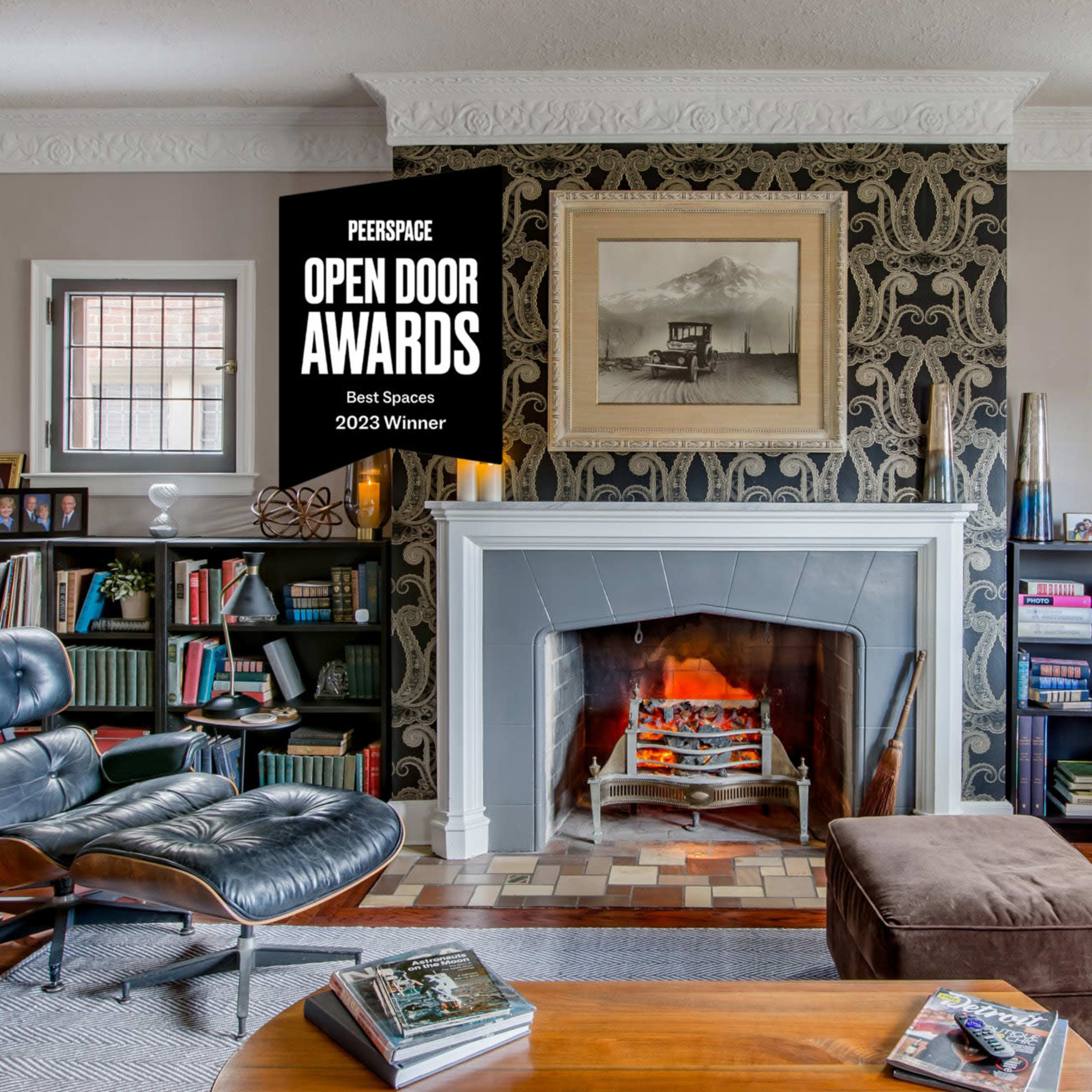 A cozy living room features a fireplace with a patterned wall behind it, surrounded by bookshelves filled with books and decorative items.