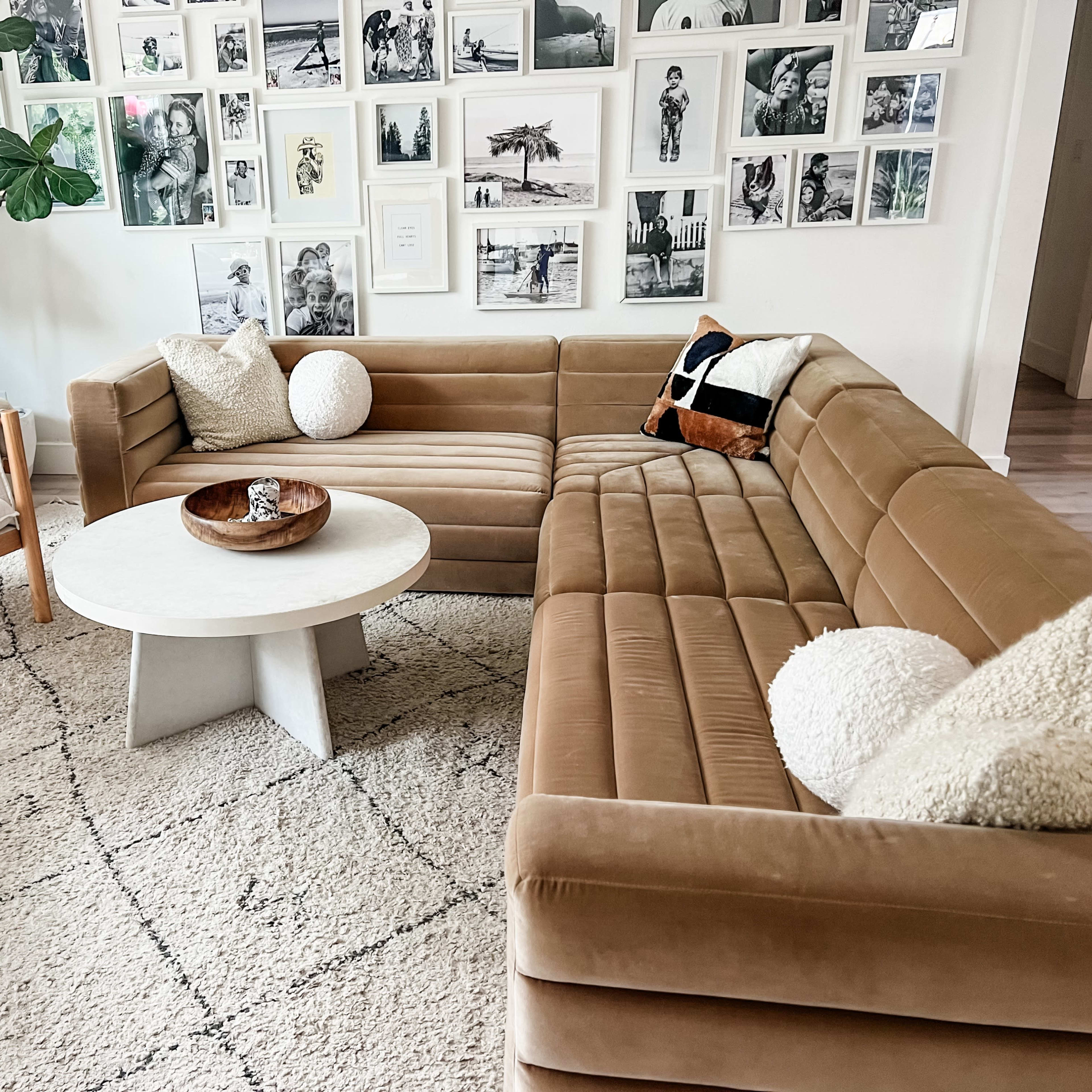 A modern living room featuring a tan sectional sofa, a round coffee table, and a wall adorned with framed black-and-white photographs.