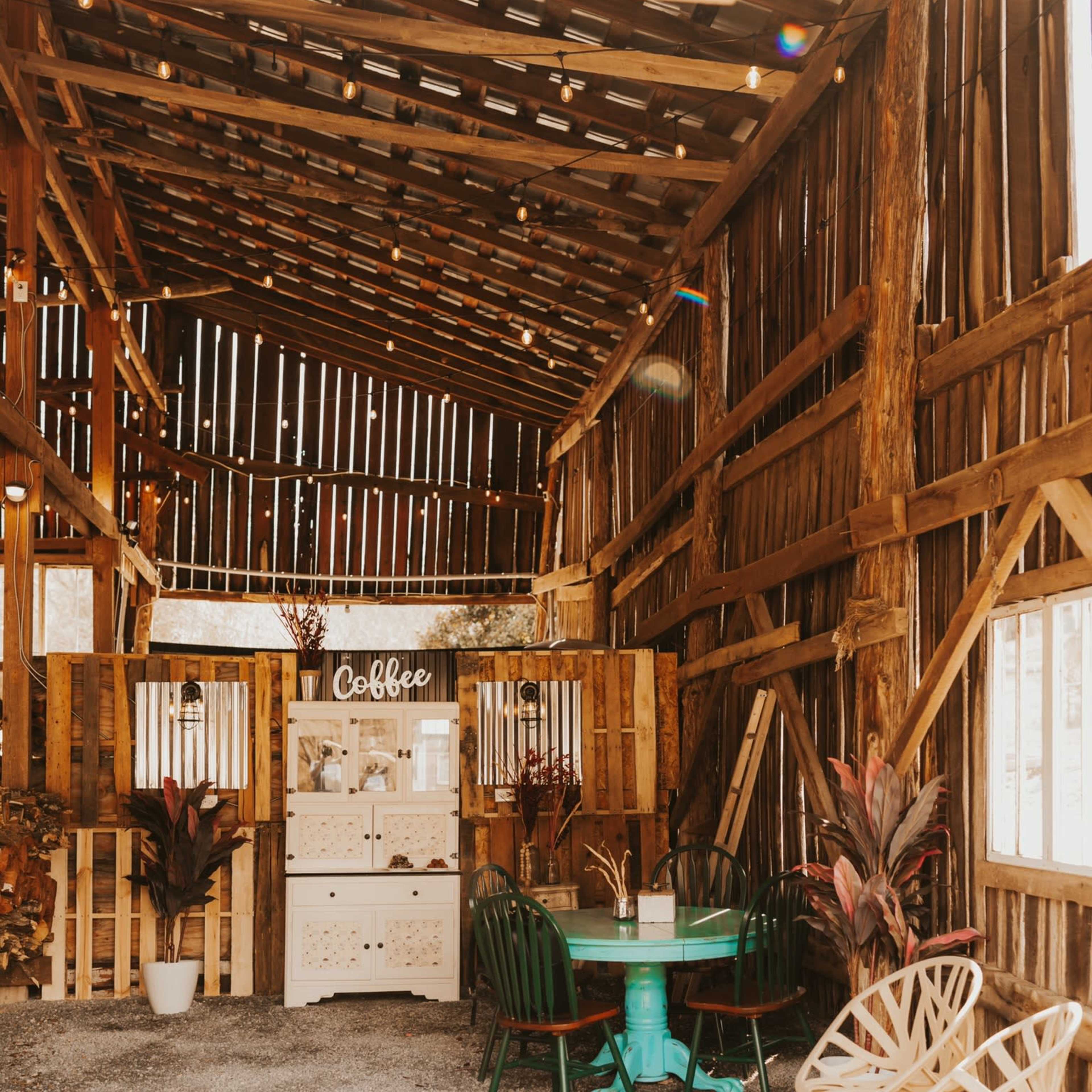 A rustic, wooden barn interior with a coffee station and seating area featuring a turquoise table and various chairs.