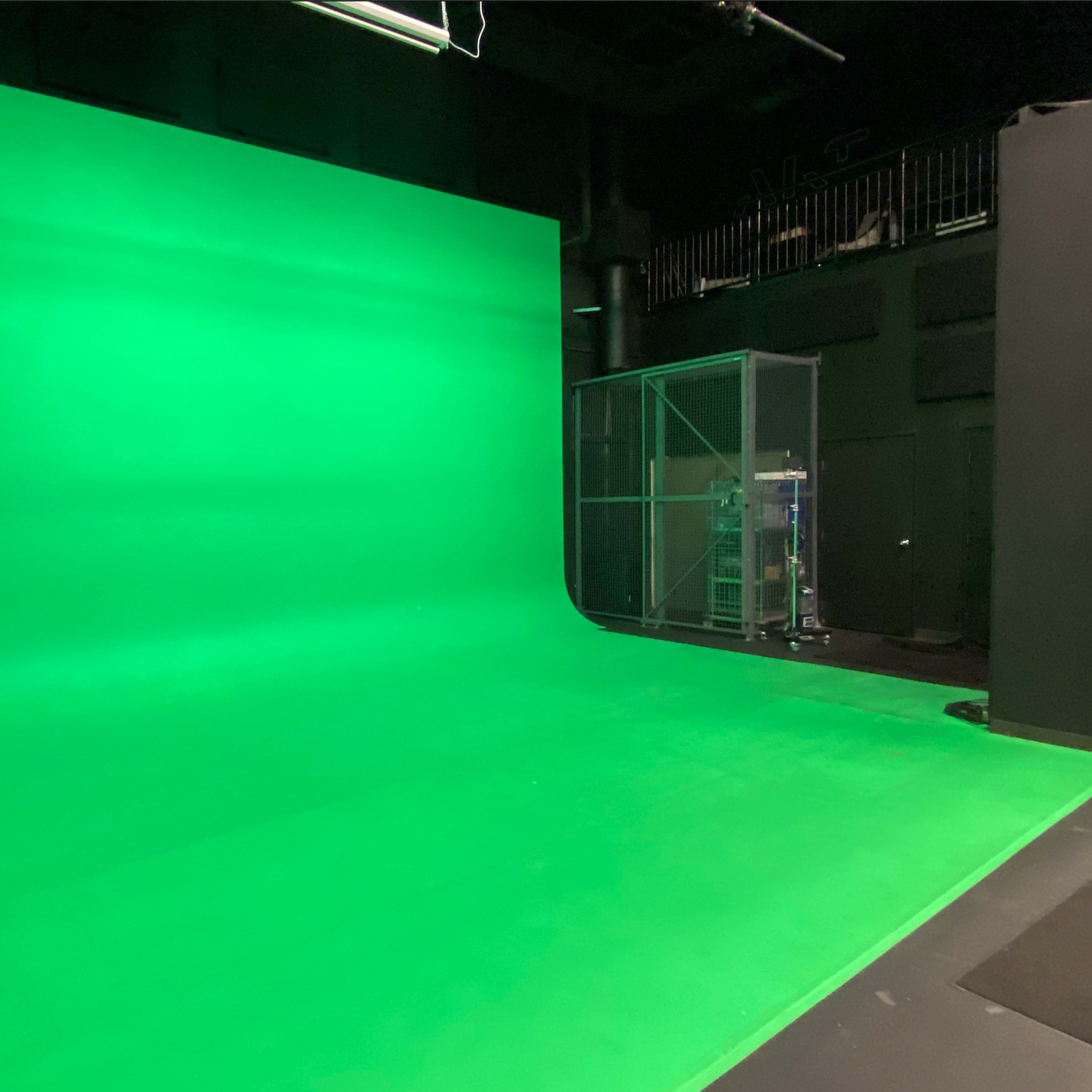 A green screen studio with a smooth green backdrop and a transparent enclosure in the corner.