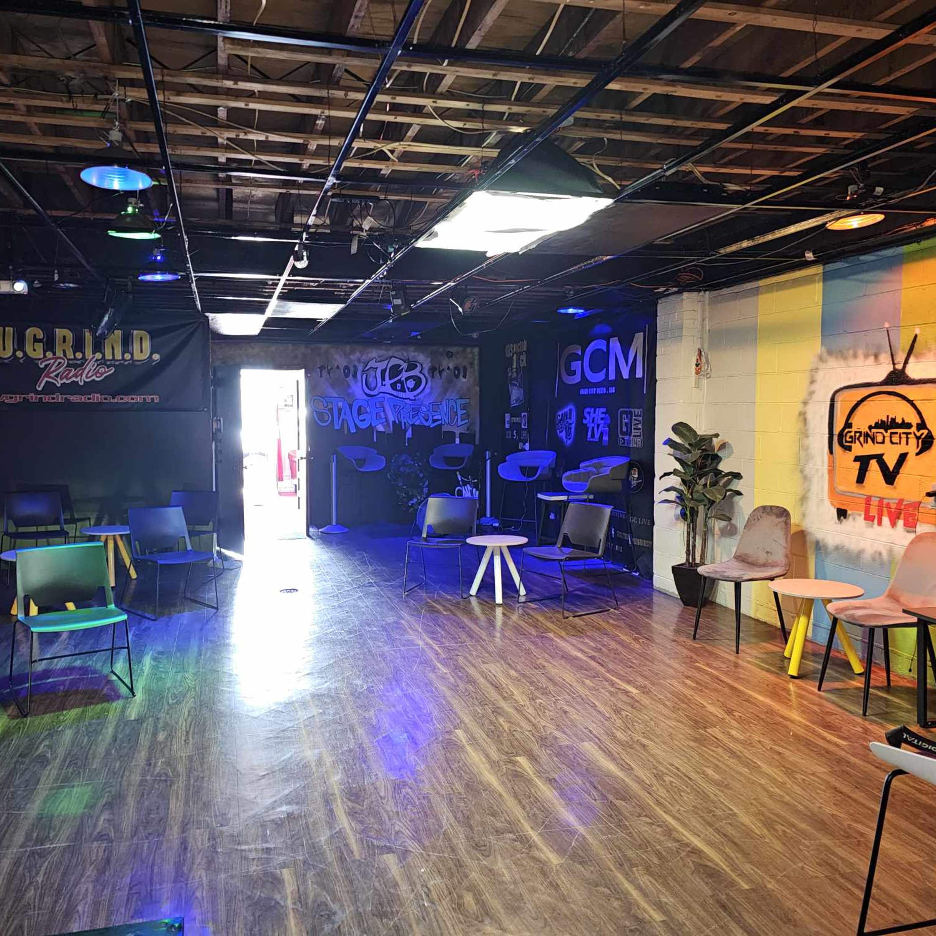 A spacious room with modern chairs and tables, featuring colorful murals and various lighting setups.