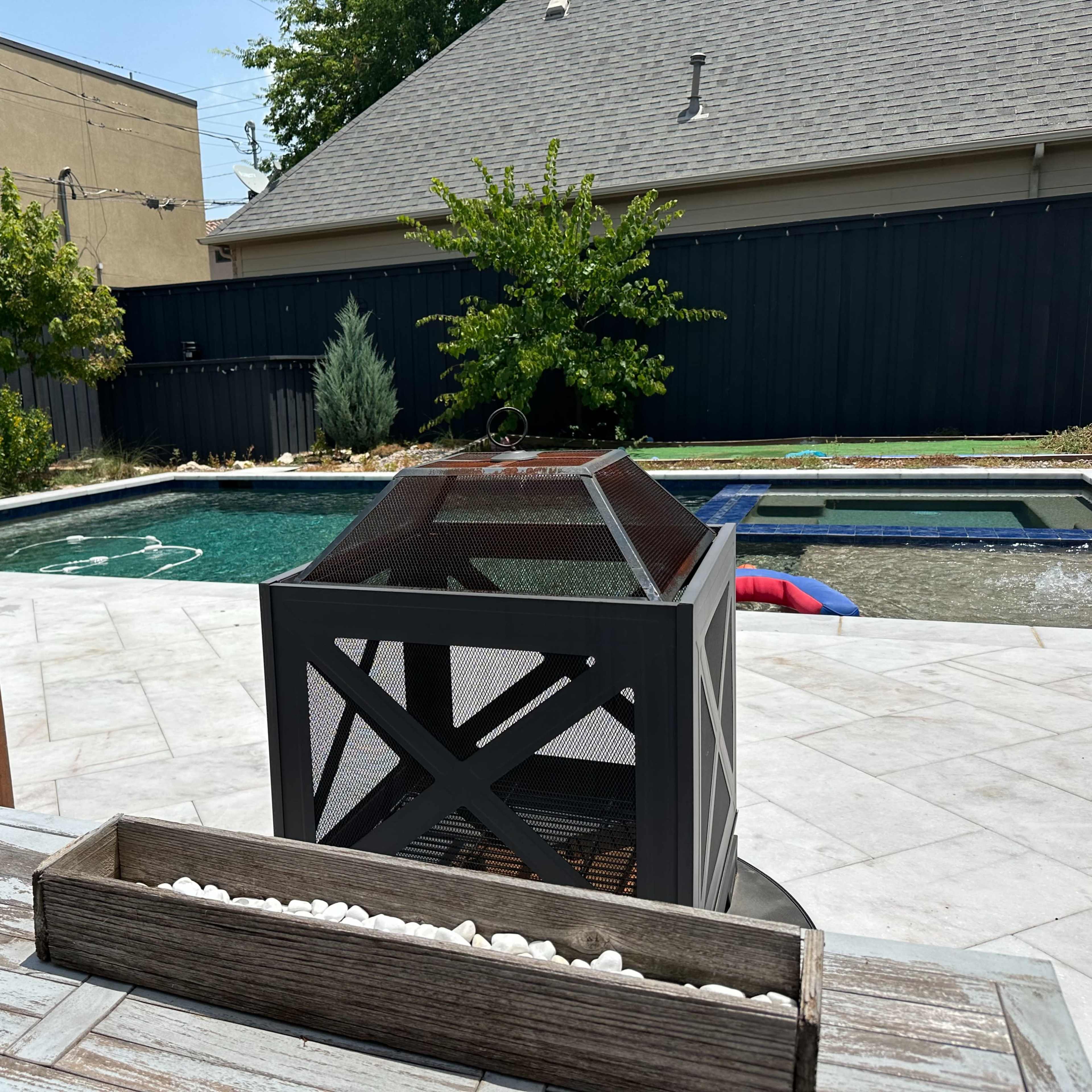 A backyard features a swimming pool surrounded by a patio, a seating area, and a fire pit.