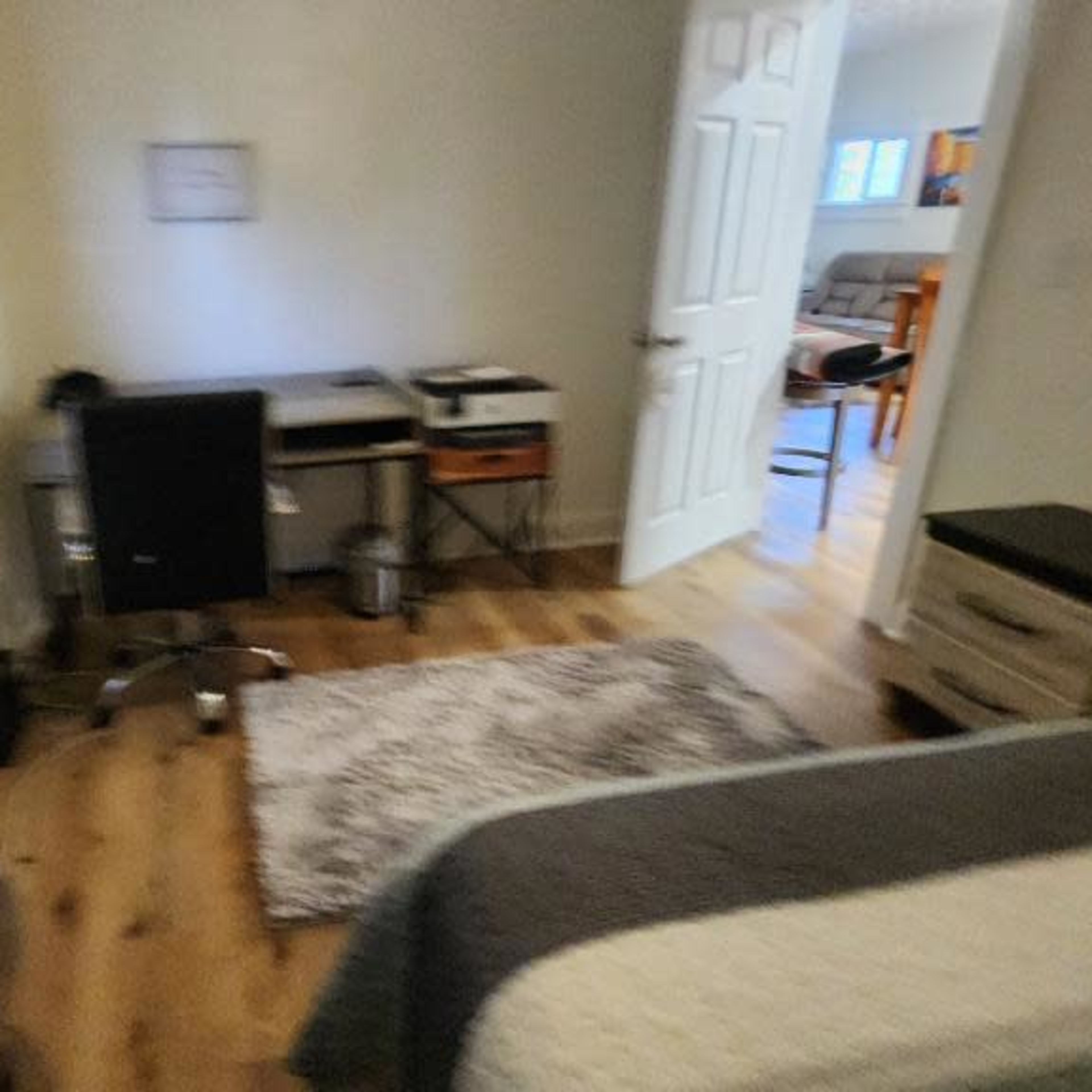 A blurred view of a small bedroom featuring a desk and chair, a television, and a doorway leading to another room.