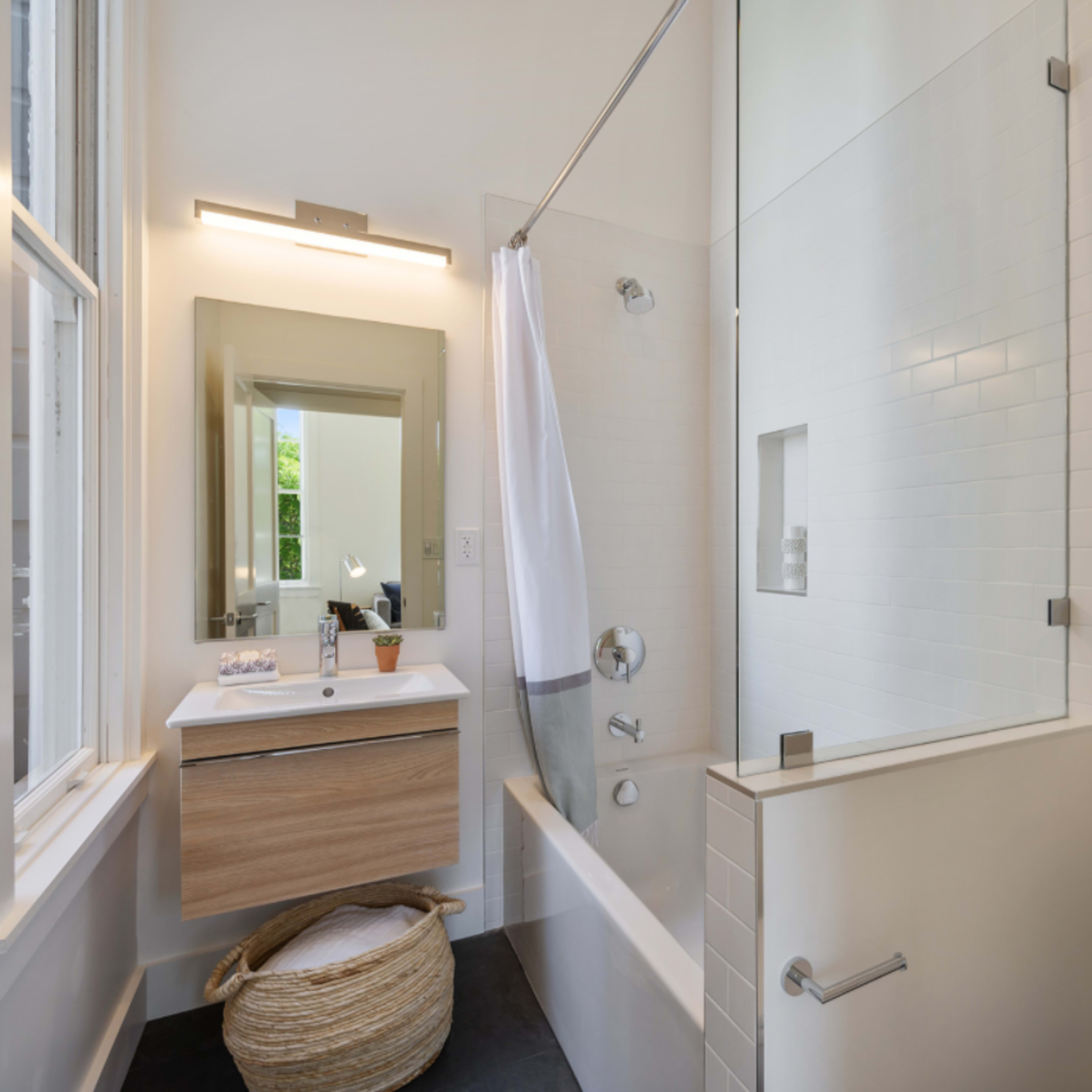 A modern bathroom featuring a glass-enclosed shower, a wooden vanity with a mirror, and a bathtub, all arranged with neutral-toned tiles and decor.
