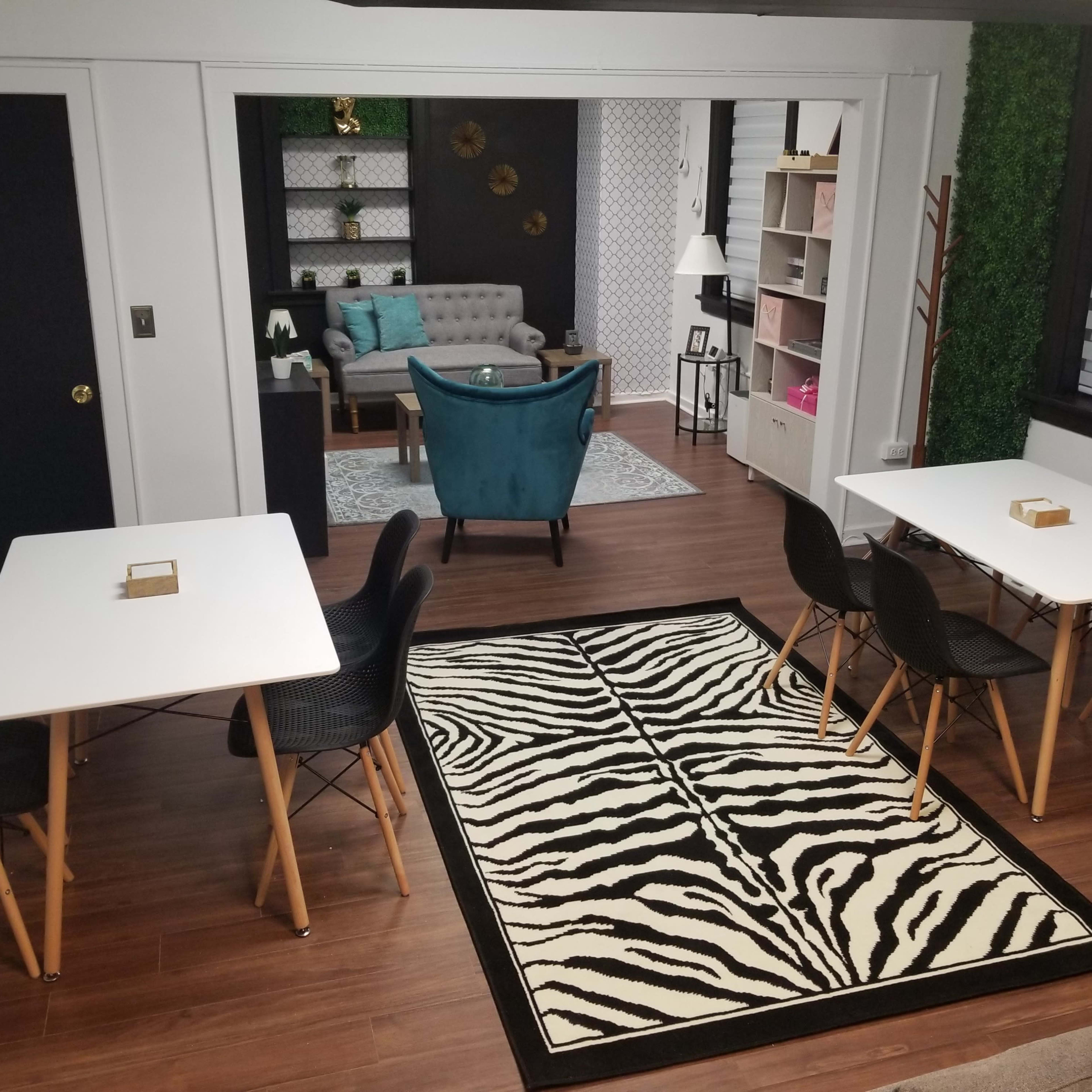 A modern interior space featuring two tables with black chairs, a zebra-striped rug, and a cozy seating area with a teal armchair in the background.