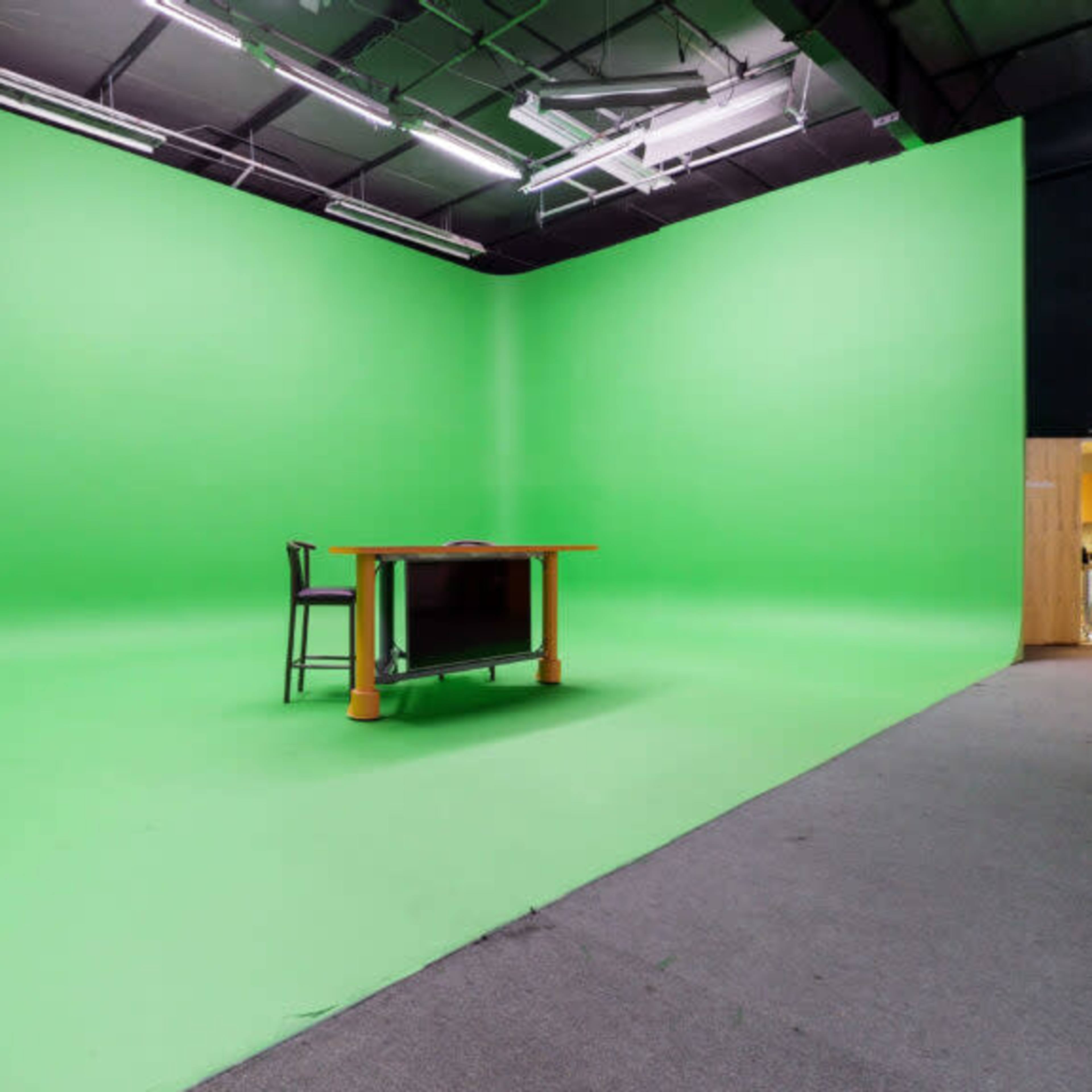 A large green screen studio with a table and chair set against a vibrant green backdrop.