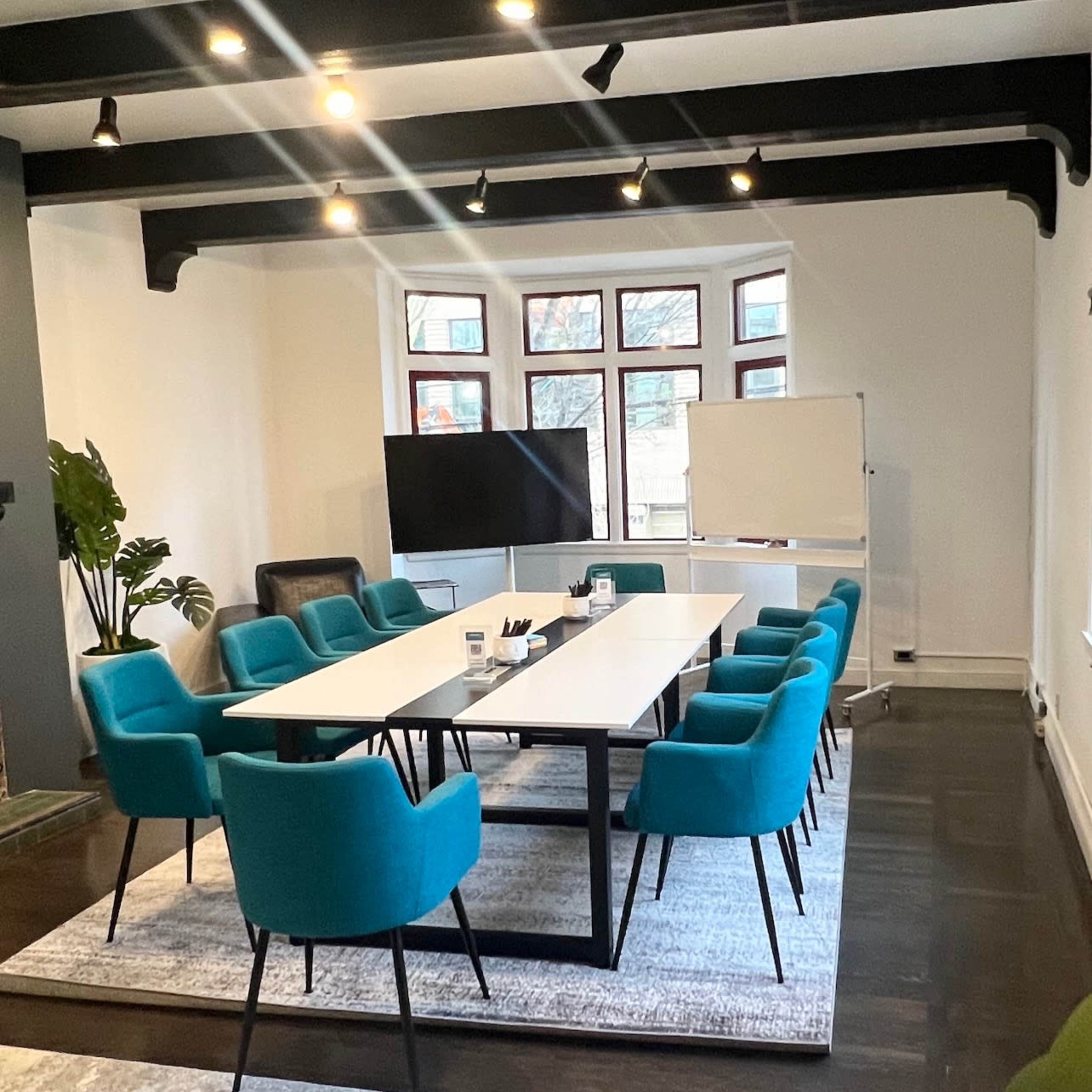 A conference room features a long rectangular table surrounded by turquoise chairs, with a television and a whiteboard in the background.