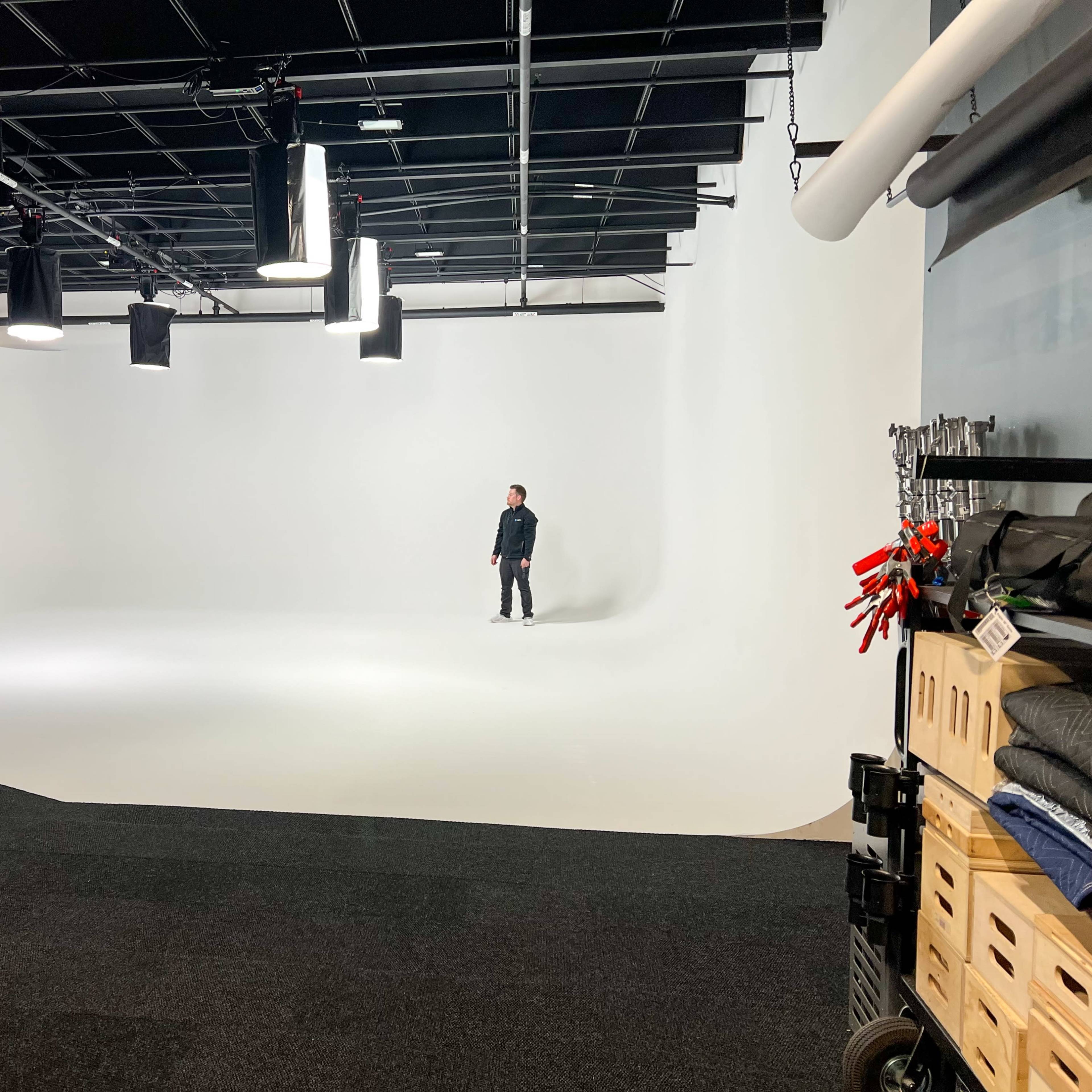 A person stands alone on a seamless white backdrop in a spacious studio.