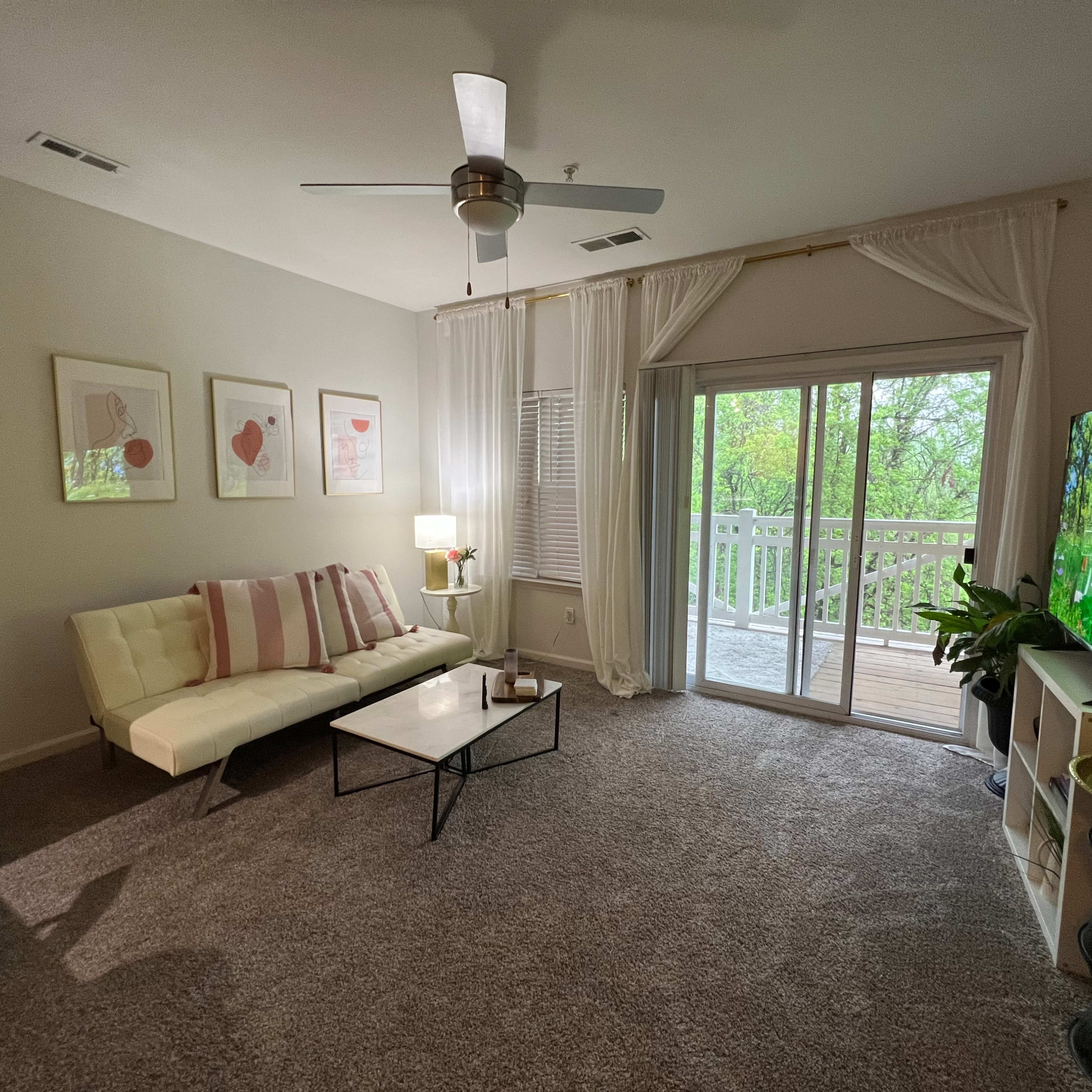 A living room features a white sofa, a black coffee table, and a large window with a sliding door leading to a balcony.