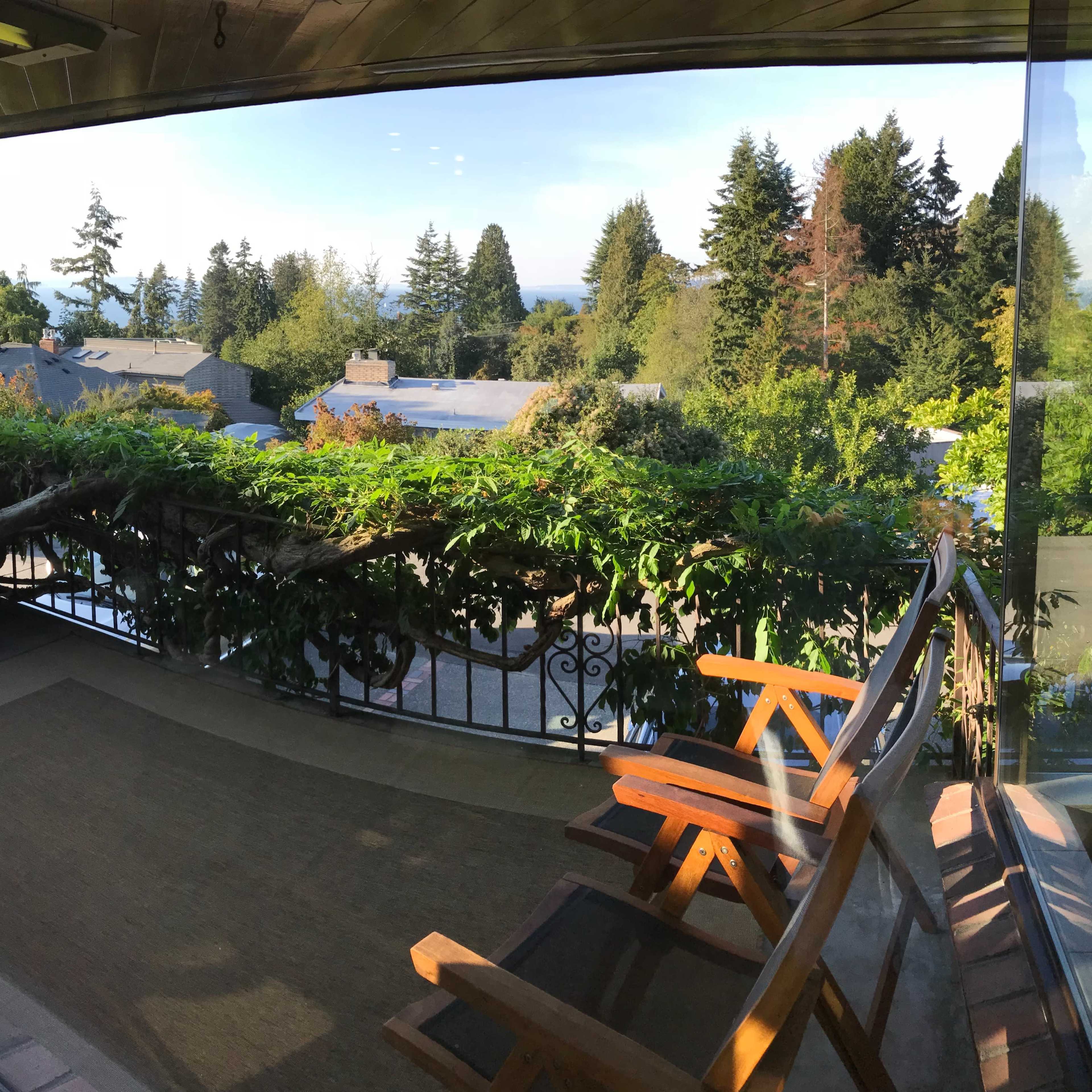 A view from a room with a wooden deck and two chairs overlooking a landscape of trees and distant water.