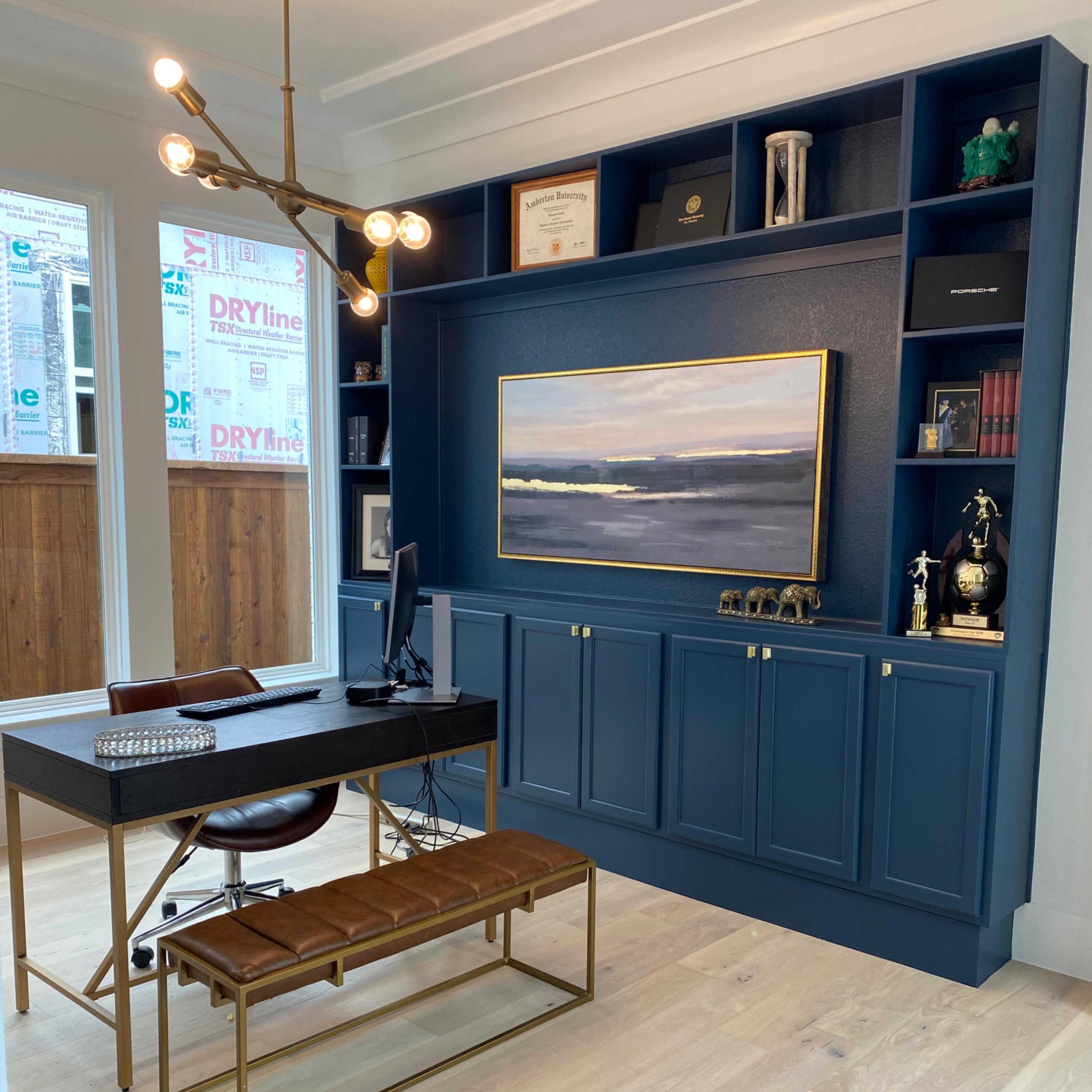A modern home office with a navy blue wall unit, a desk with a computer, and decorative items including trophies and books.