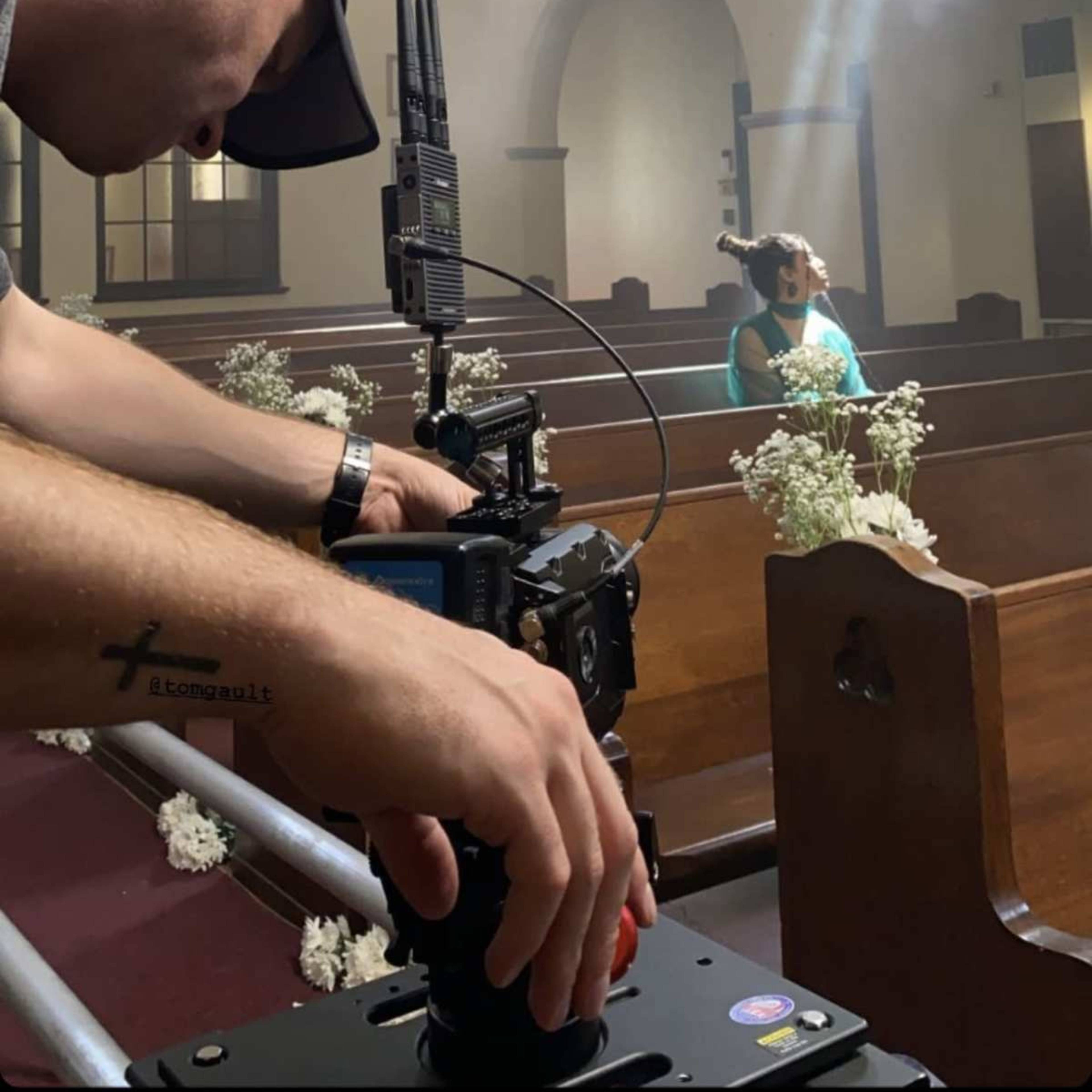A person operates a camera in a church while a child stands in a pew, illuminated by rays of light.