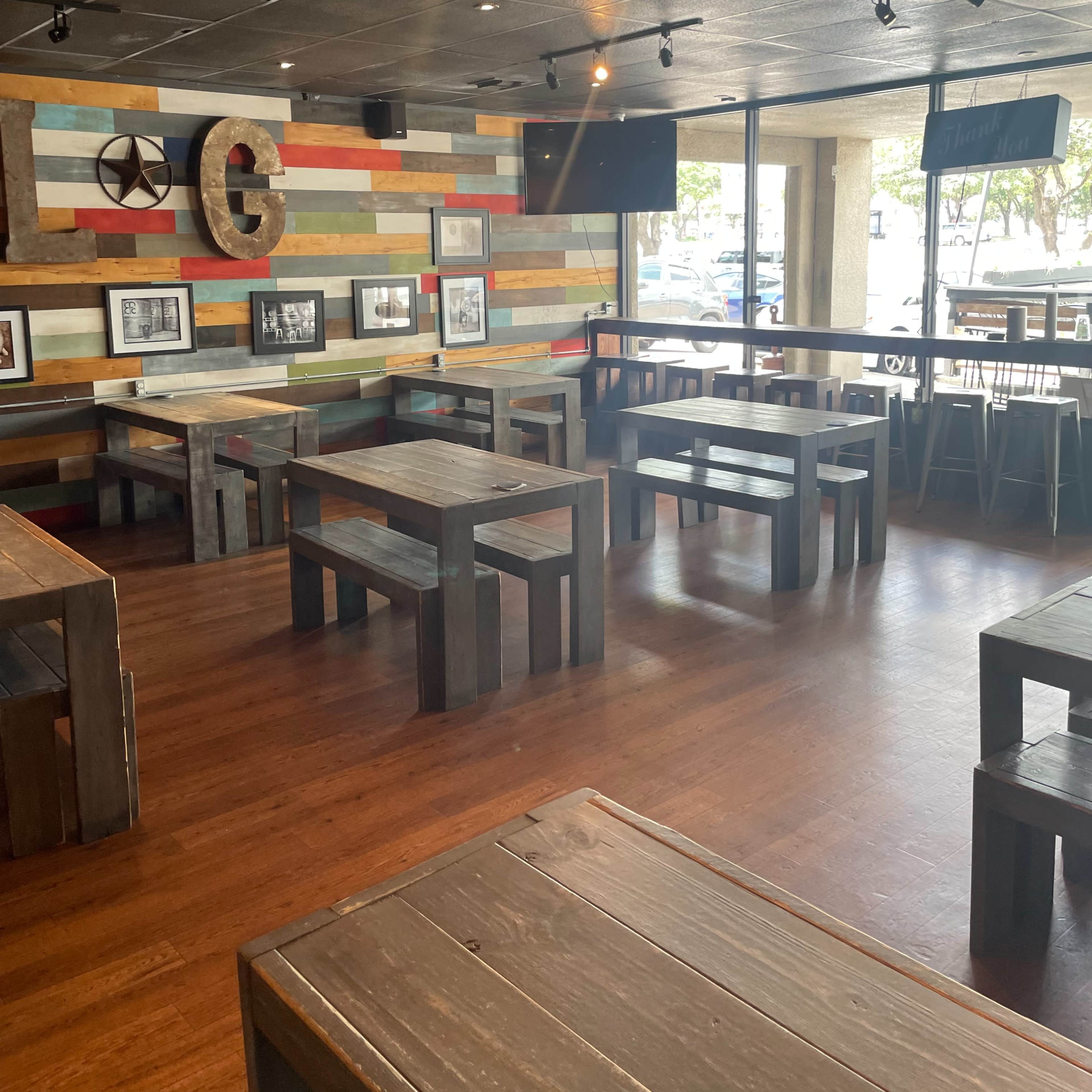 An empty modern restaurant with wooden tables and a colorful accent wall featuring framed photographs.
