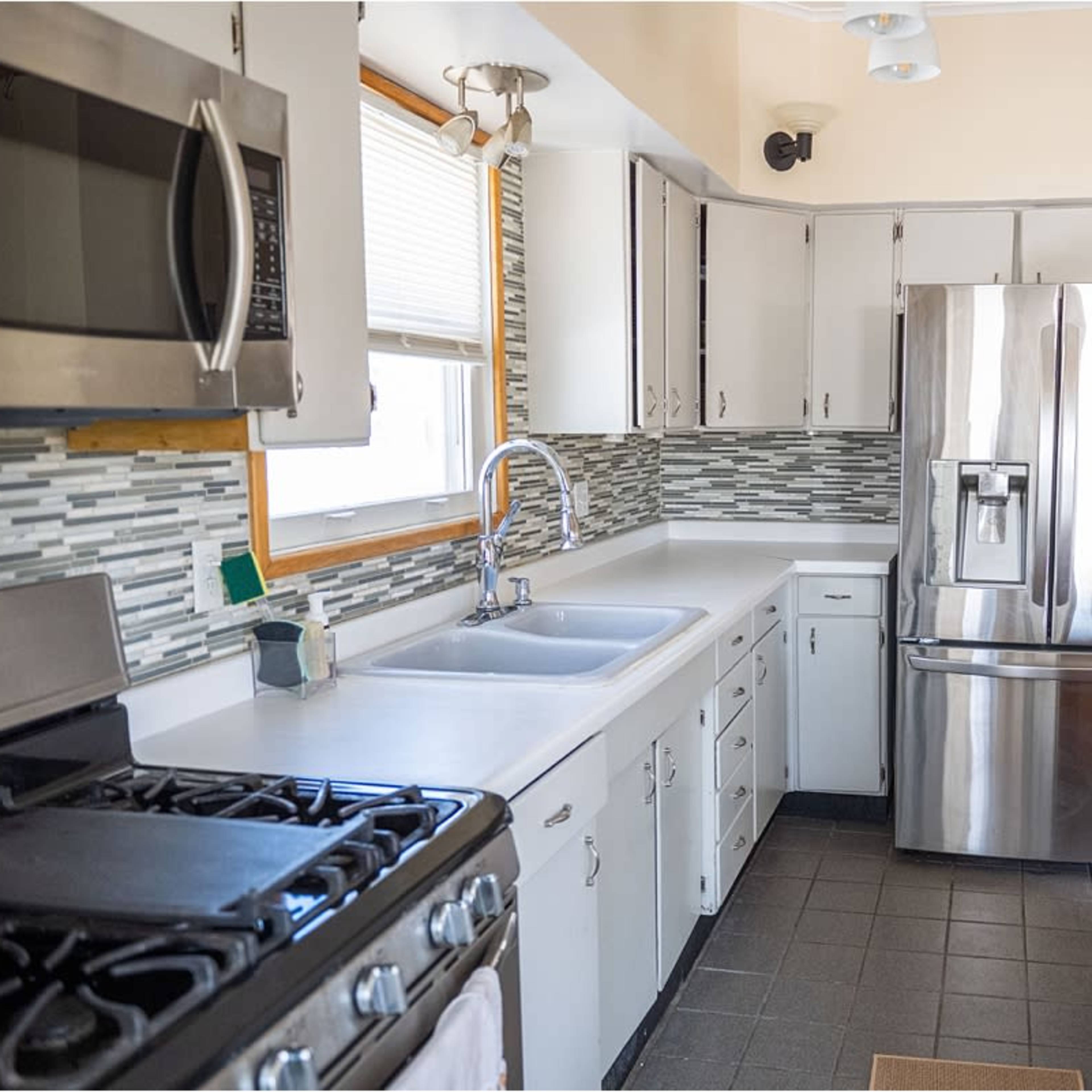 A modern kitchen featuring stainless steel appliances, a white countertop, and tile backsplash in shades of gray.