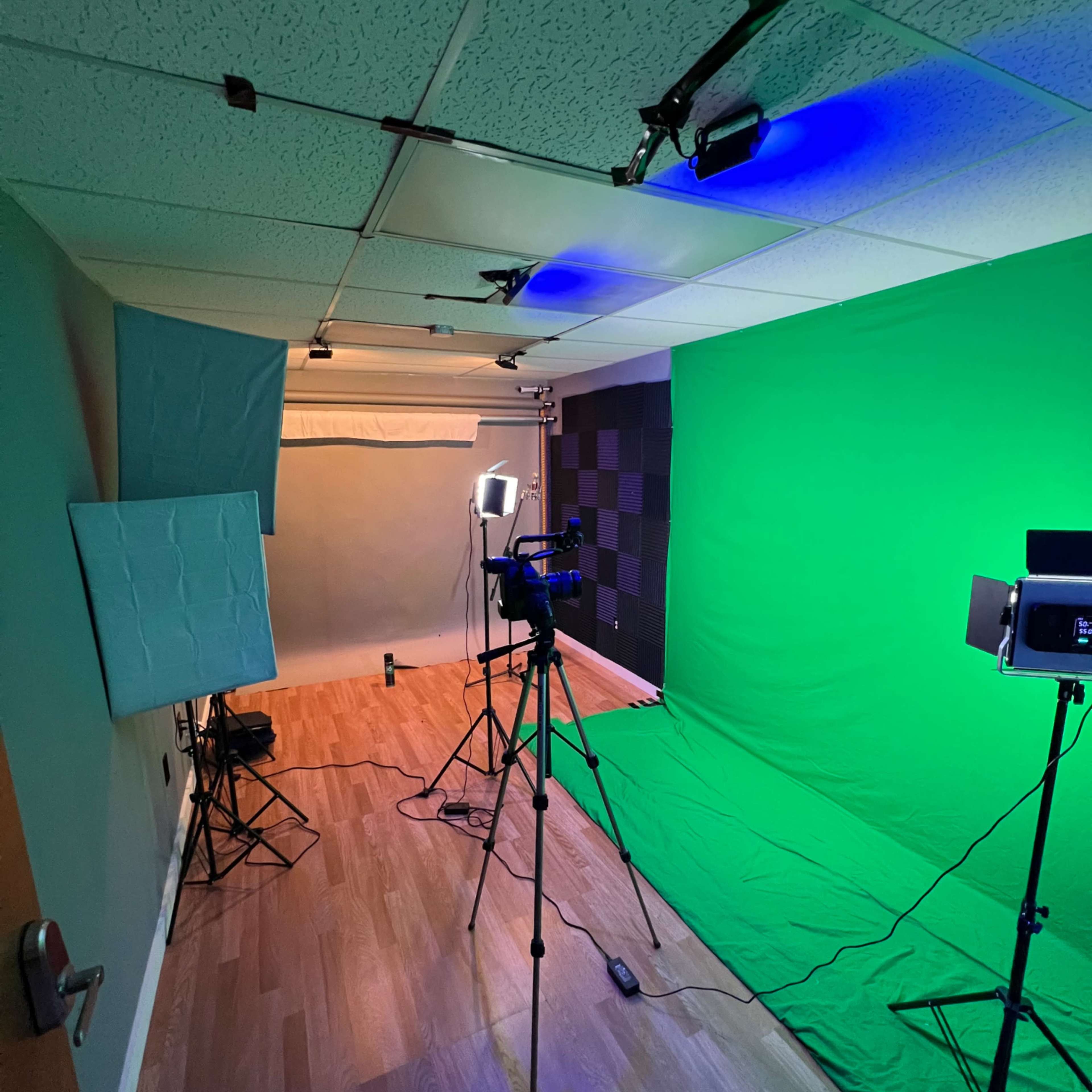 A recording studio setup featuring a green screen, lighting equipment, and a camera on a tripod.